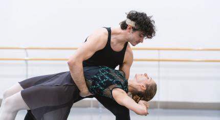 A dancer leans back horizontal help by another supporting her while looking into her eyes