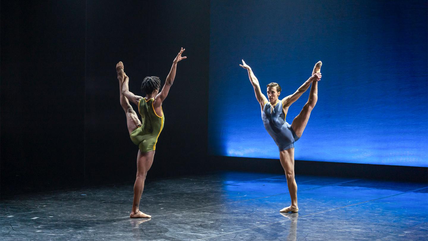 Mlindi Kulashe and Andrew Tomlinson face each other as they reach high with one arm whole holding their left leg aloft with the other