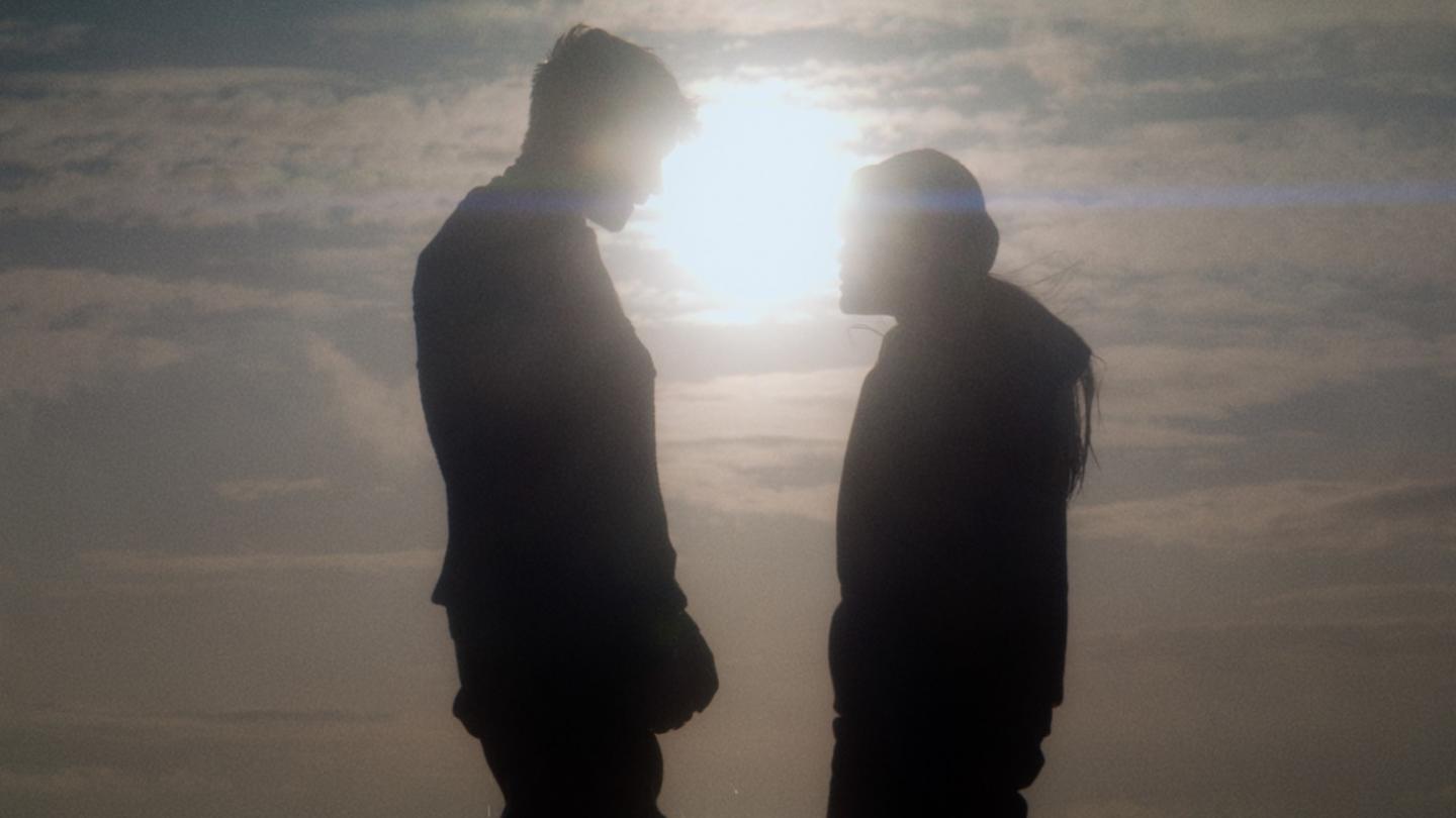 Two people stare at each other as the sun sets behind them