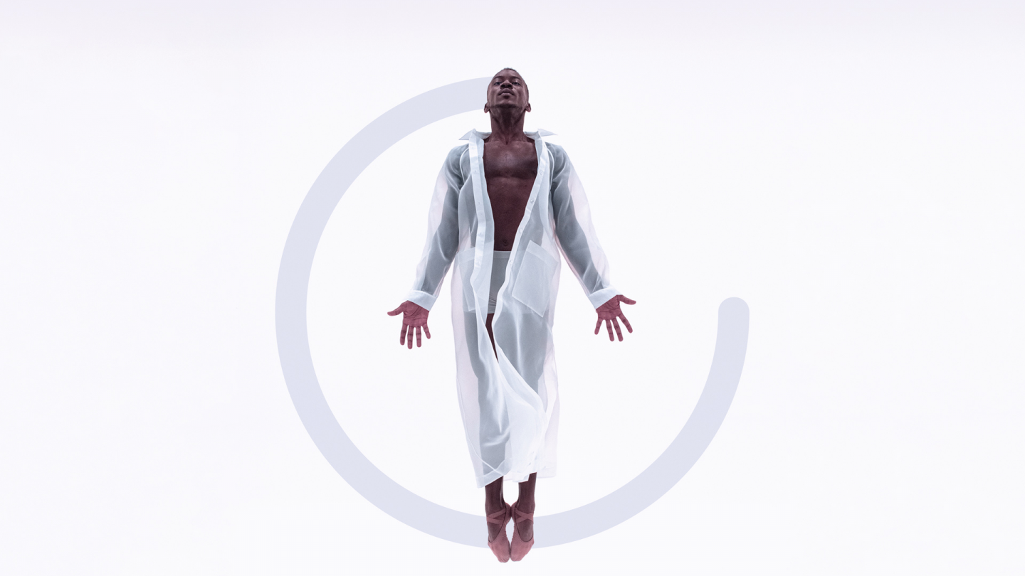 A man is floating in the air wearing a sheer white jacket, which is long sleeve and goes down to their ankles. The are looking up towards the sky with their palms faced to the front. There is a grey semi-cirle graphic added to the image behind the dancer.