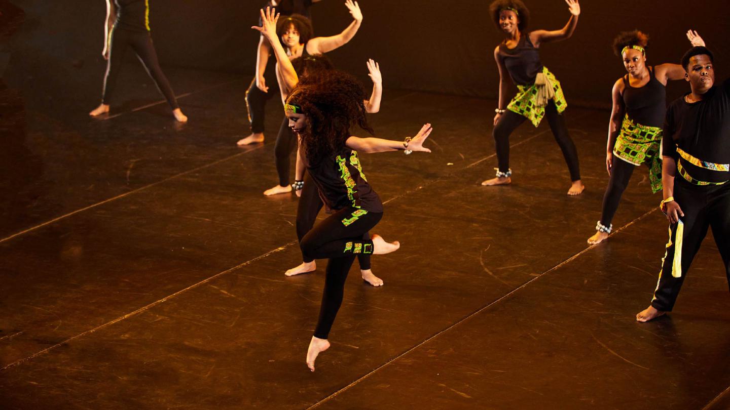 A group of dancers dressed in black with green and black patterned highlights performing on a dance stage