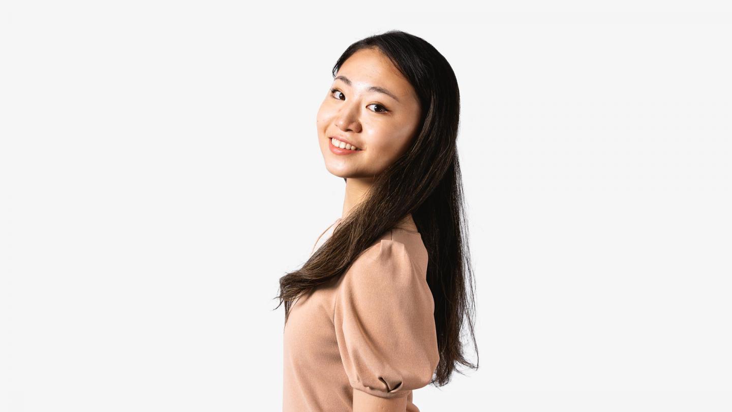 A headshot of a woman looking forward with dark brown hair and a peach coloured top