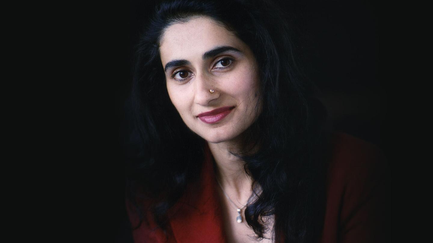 Portrait of shoulders and head of a woman with long dark hair cascading over her shoulders, a nose piercing, a dark red jacket, and dark, warm eyes.