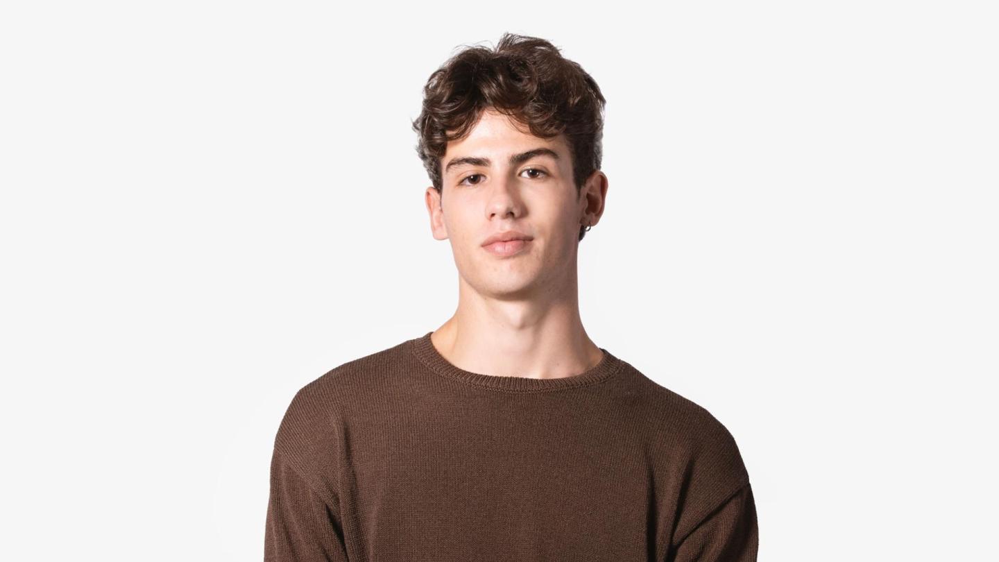 A headshot of a man with dark hair in a brown jumper stood facing the camera