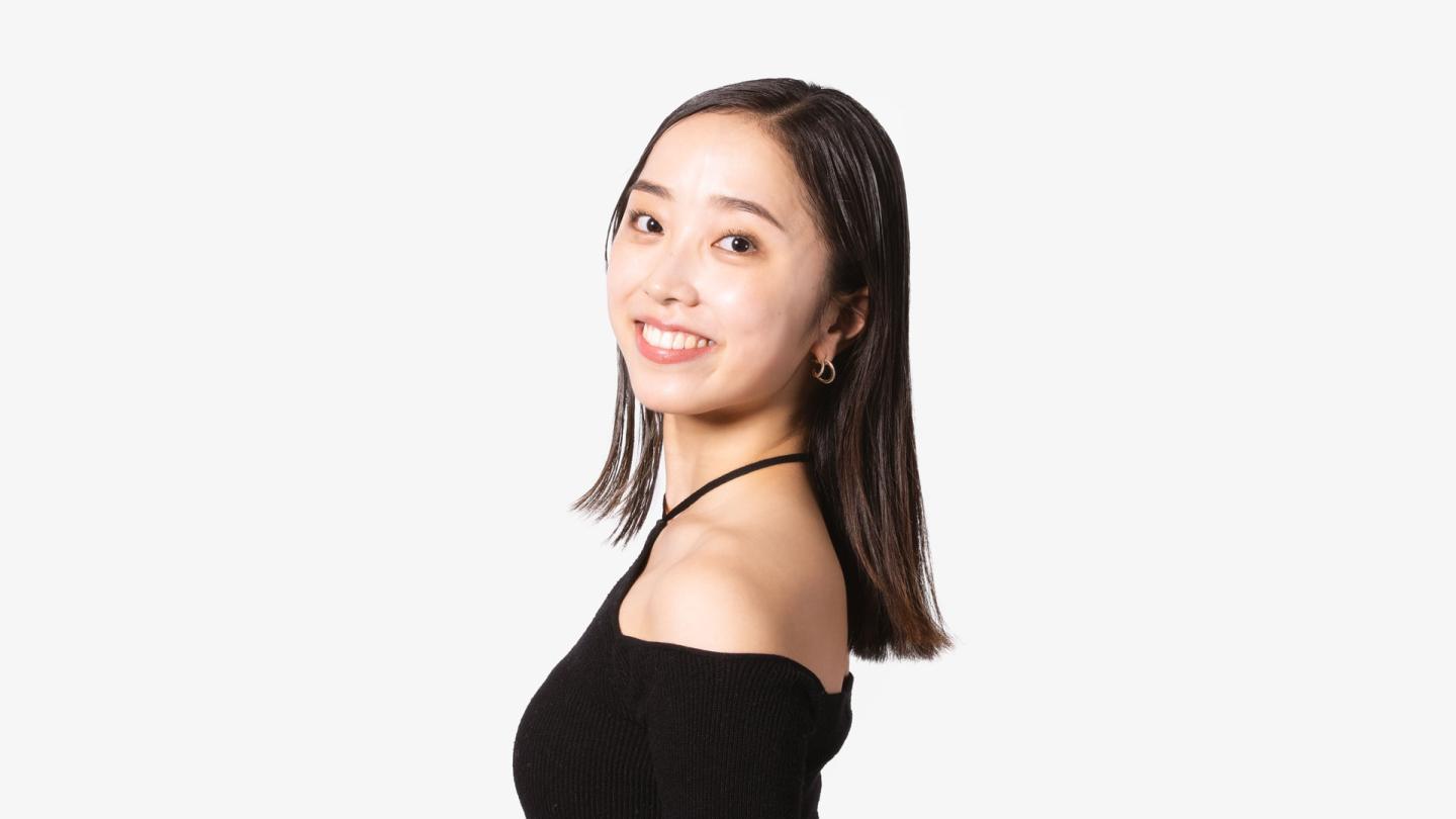 A dancer stood side on, looking at the camera wearing a black top and dark hair.