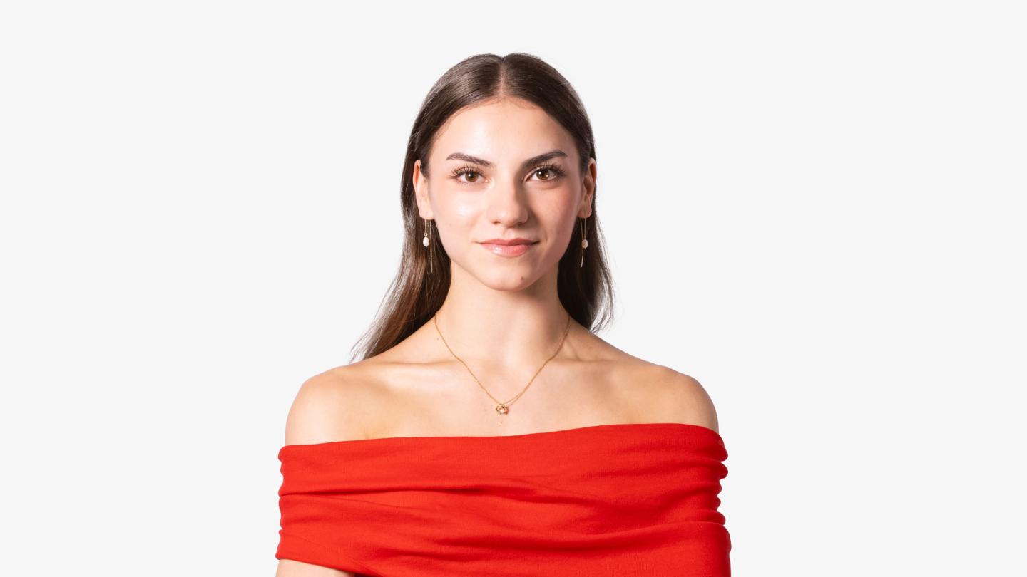 Woman with long, straight, dark hair, wearing a vivid red top, looks directly at the camera