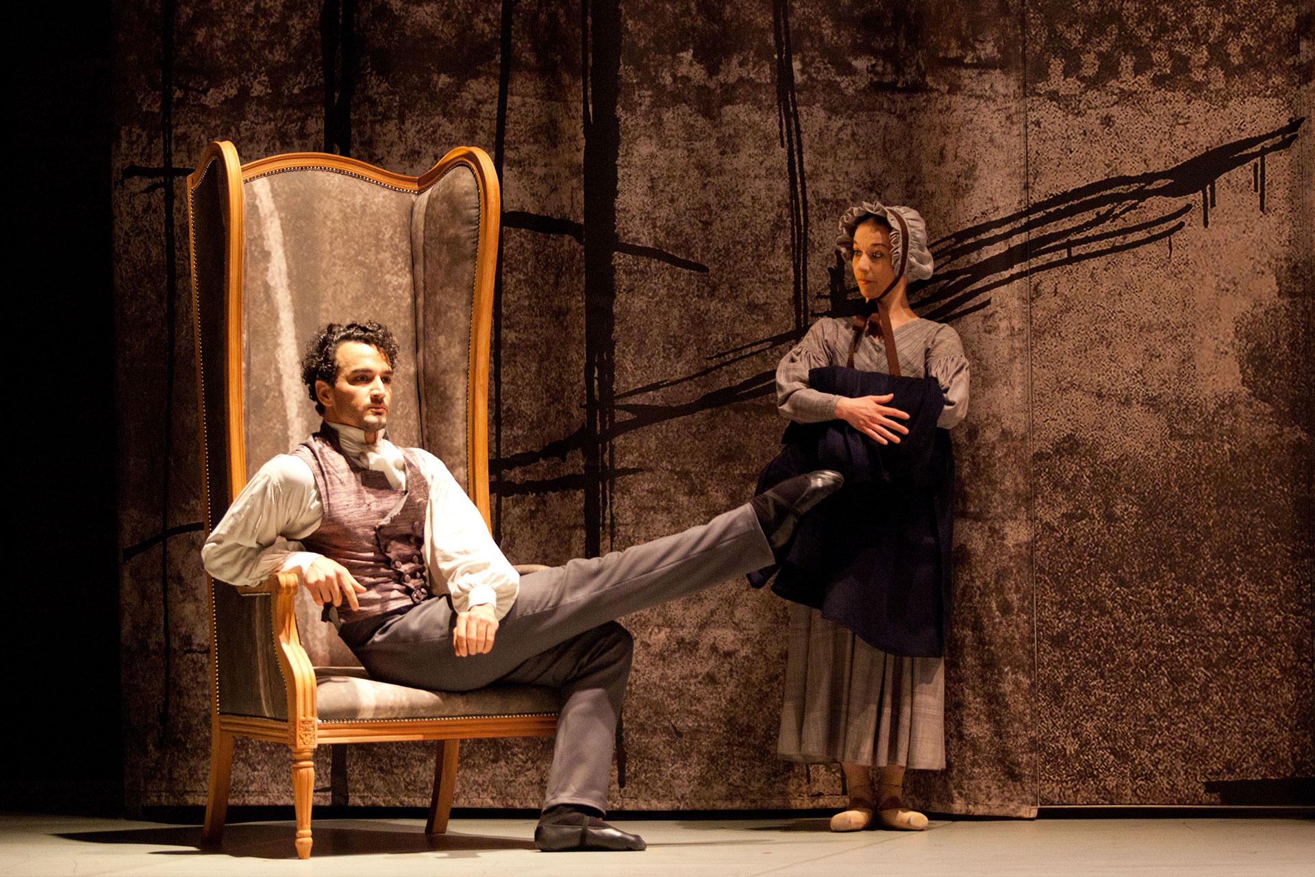 Jane Eyre, production, 2016, Javier Torres and Pippa Moore, Rochester and Mrs Fairfax, photo Caoline Holden Heathcliff extends his leg while sat in his chair while Mrs Fairfax patiently looks on