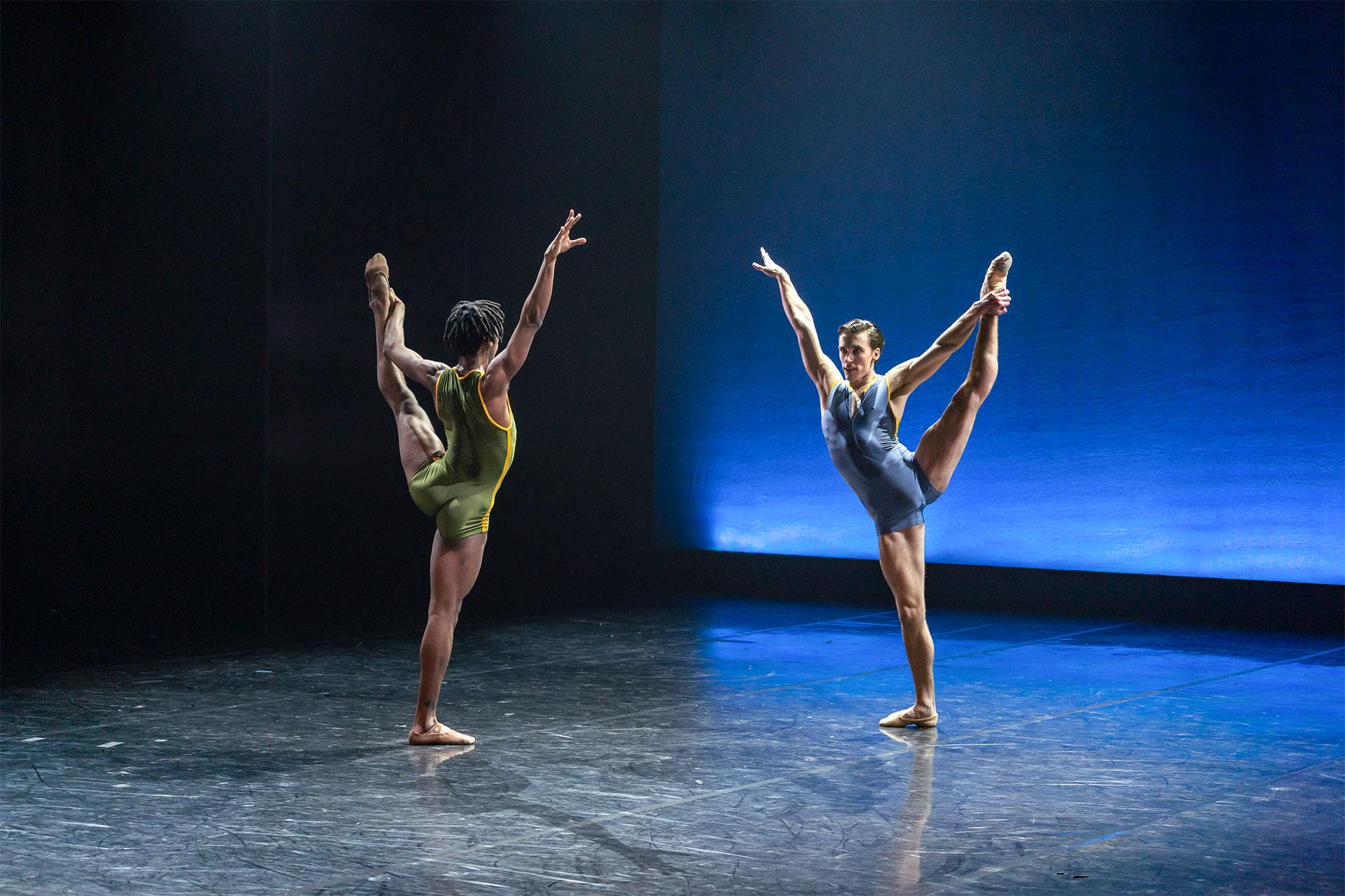 Mlindi Kulashe and Andrew Tomlinson face each other as they reach high with one arm whole holding their left leg aloft with the other