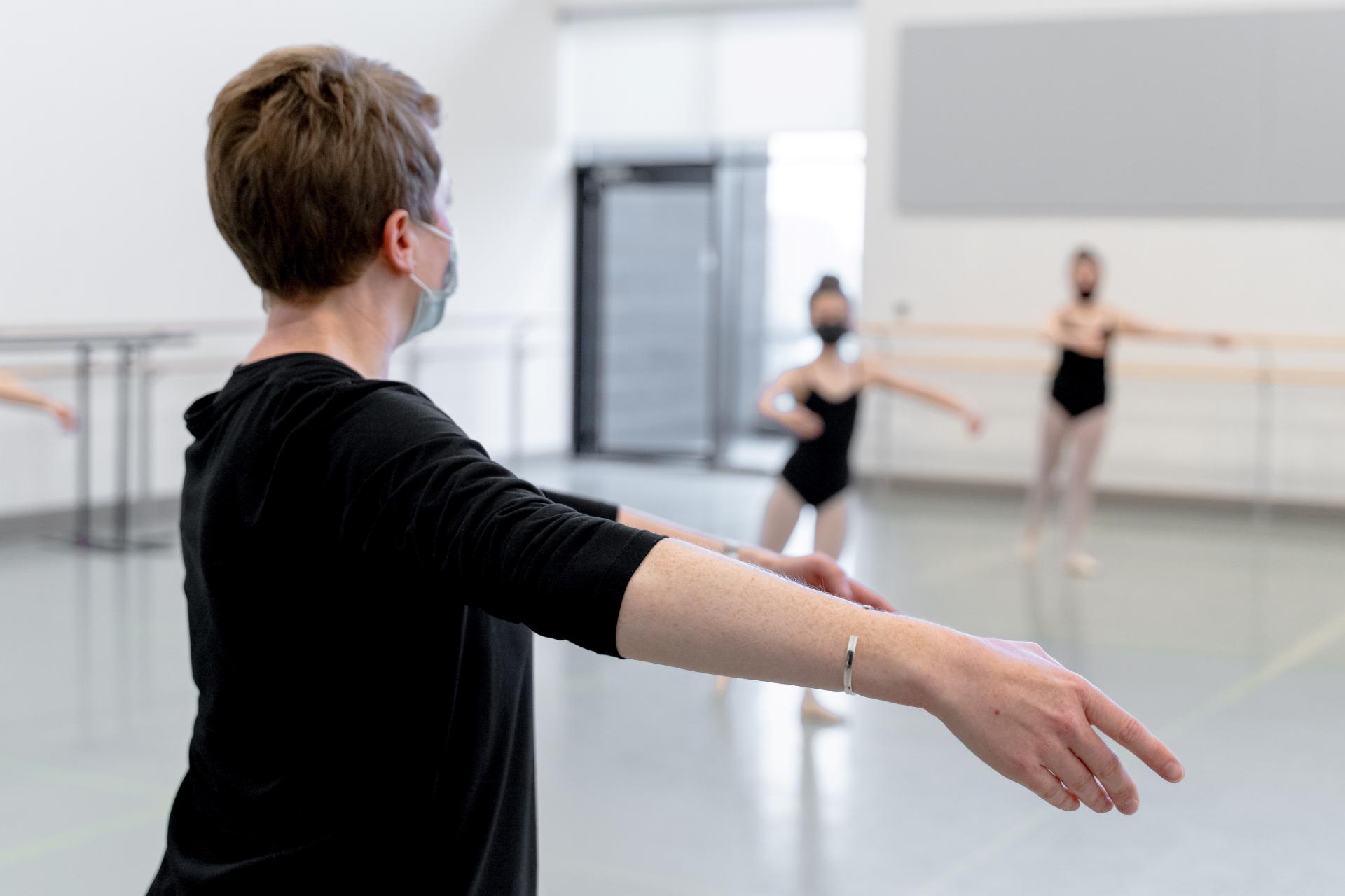 A female dance teacher wearing a face mask leads a dance class