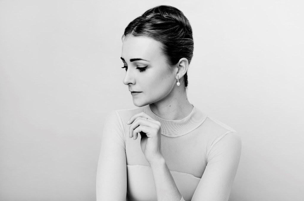 Black and white portrait of a woman looking over her right shoulder with her eyes slightly closed and one hand raise towards her chin