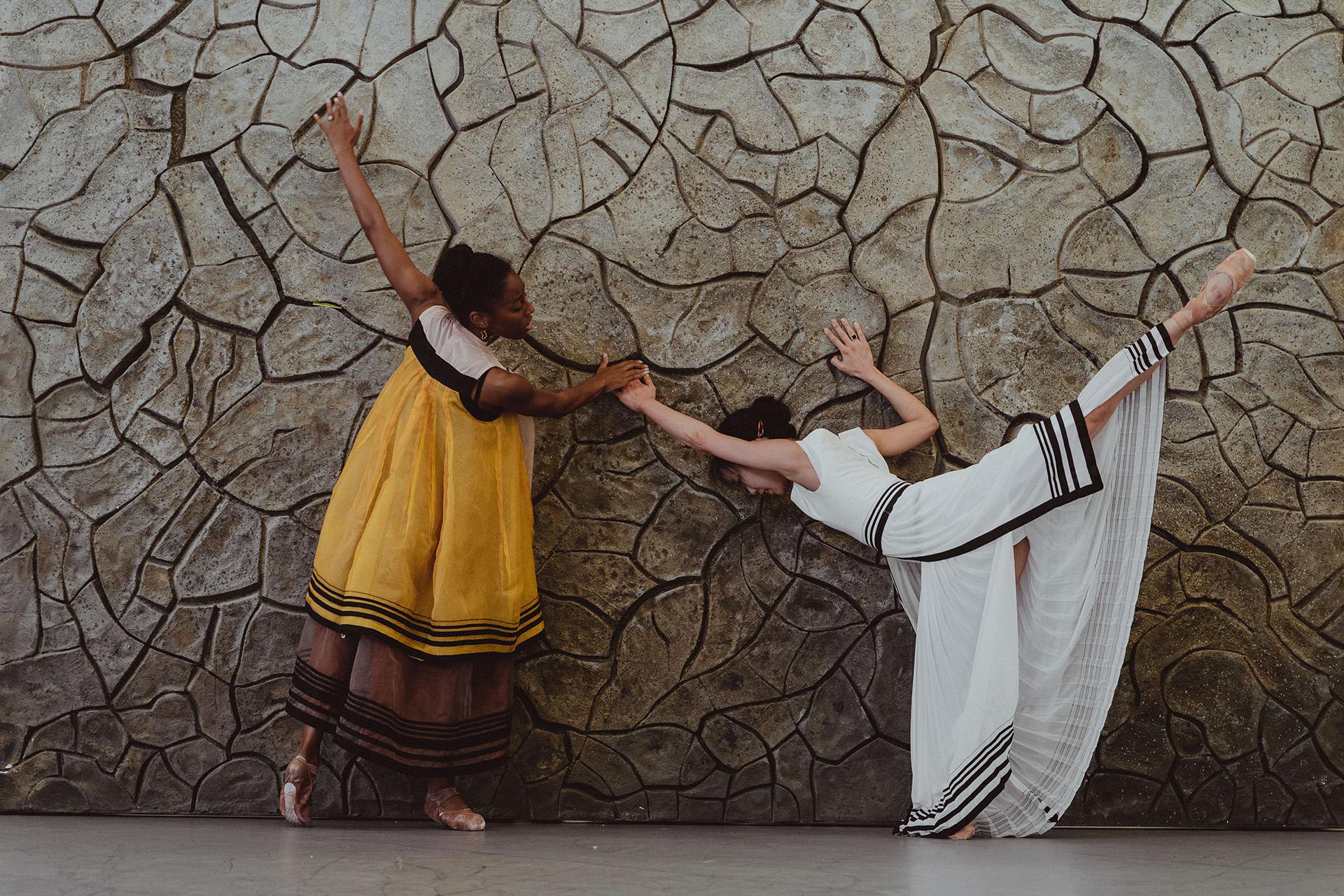Two female dancers reach out to a cracked wall