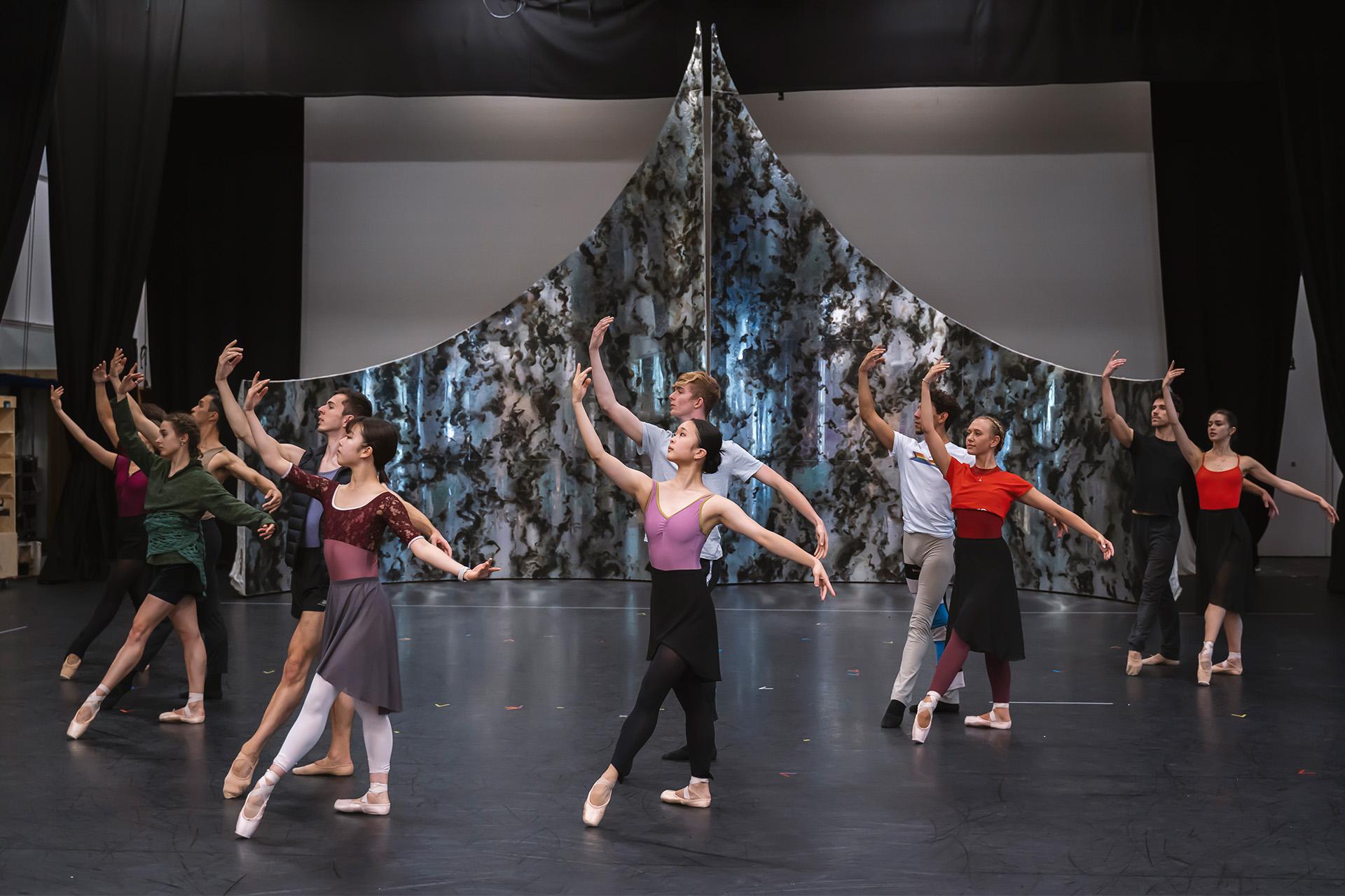 A group of dancers in rehearsal clothes stand in a uniform pose