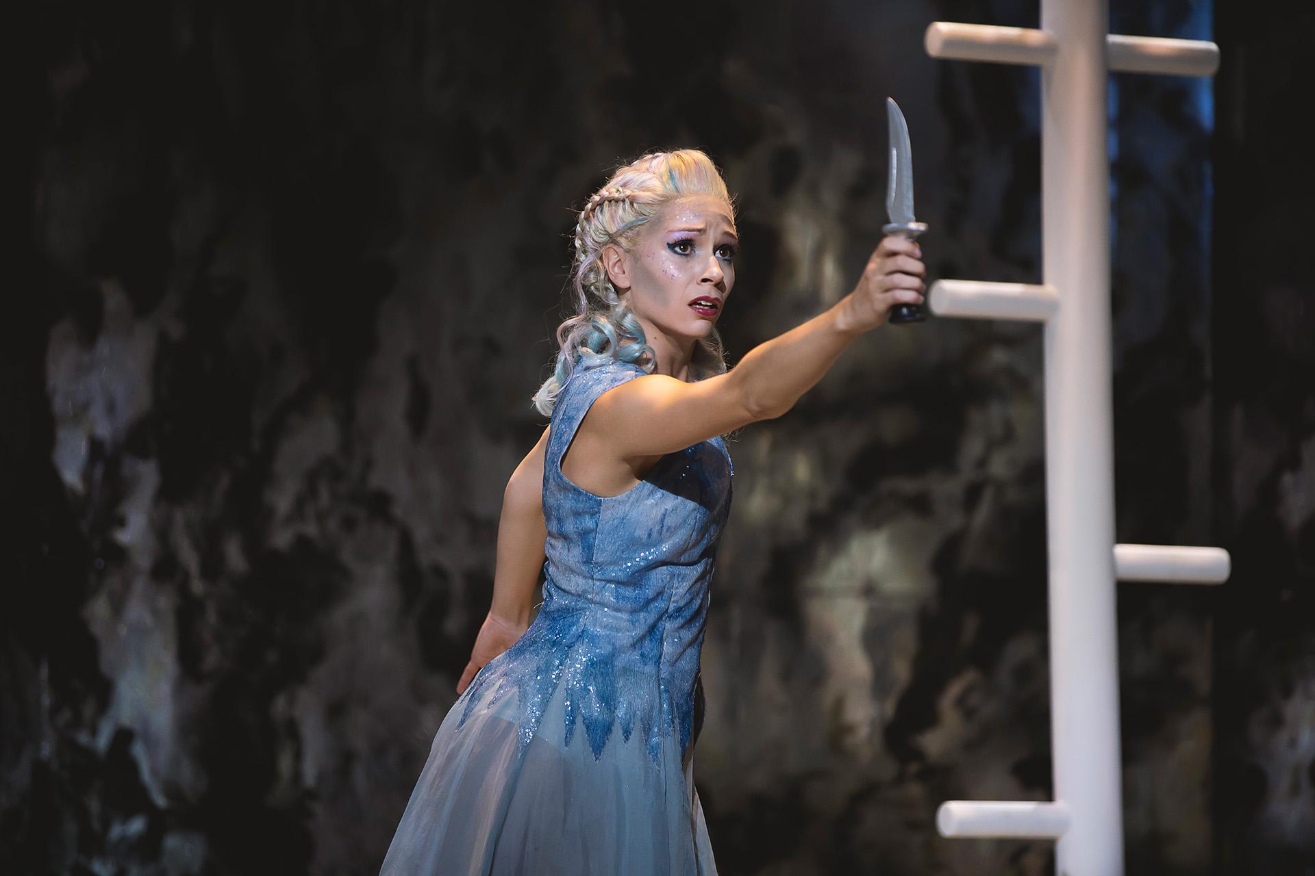 Wearing a blue dress, Marilla holds a knife in front of her