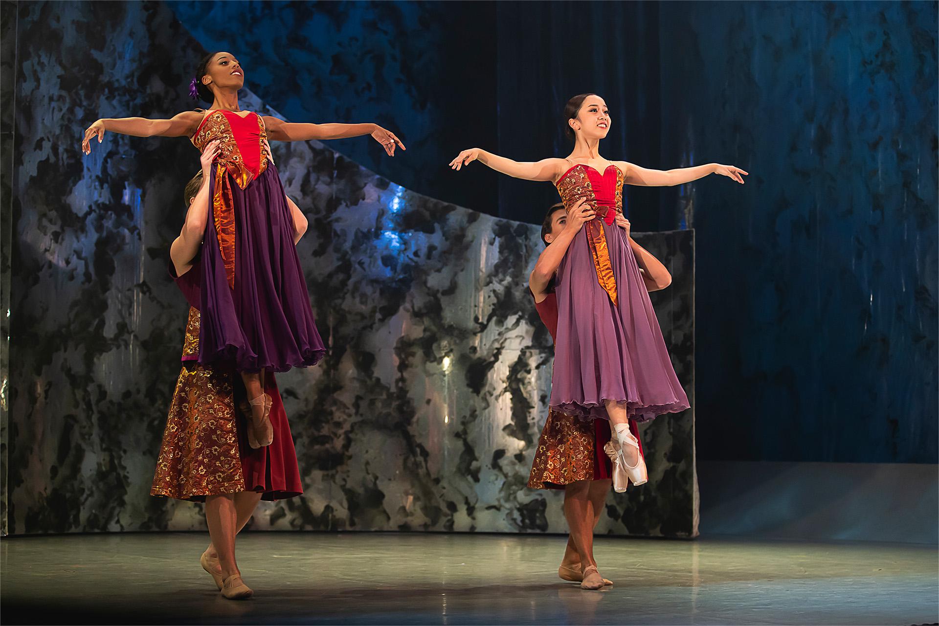 Two men wearing kilts hold two women in pointe shoes and colourful dresses aloft