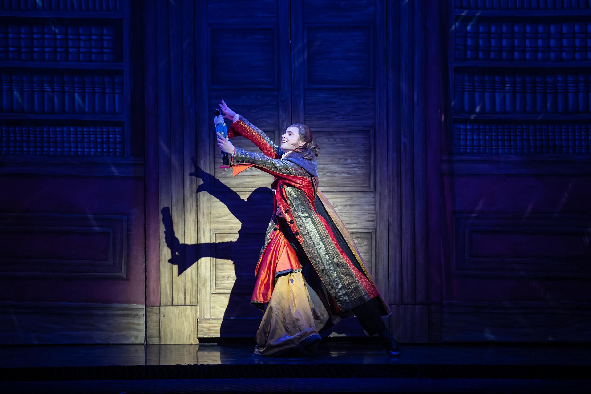 Dancer dressed in a long coat holding a soldier-shaped nutcracker doll in front of him