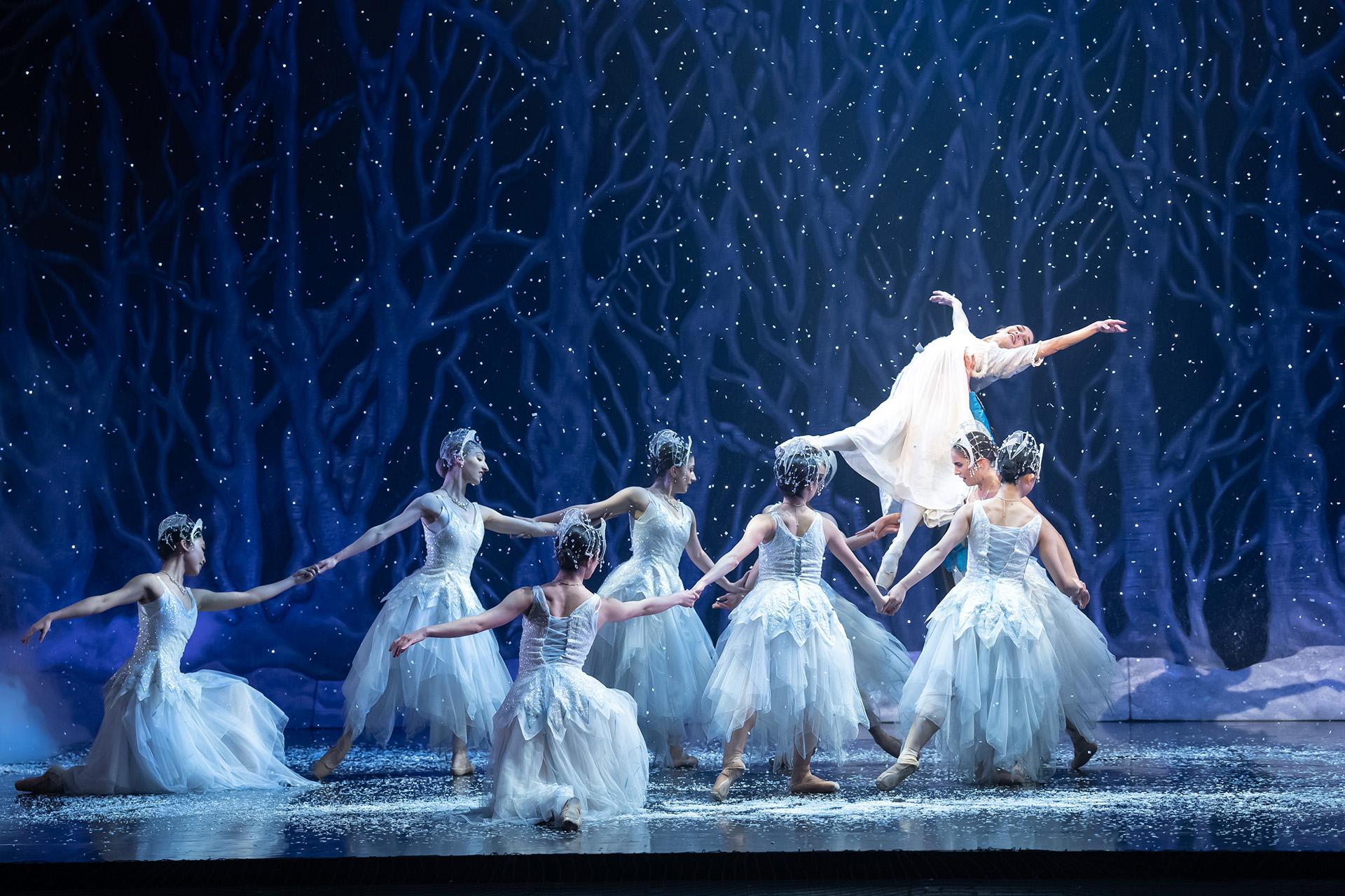 Dancers dressed in white in a whiter scene hold a young, happy woman aloft