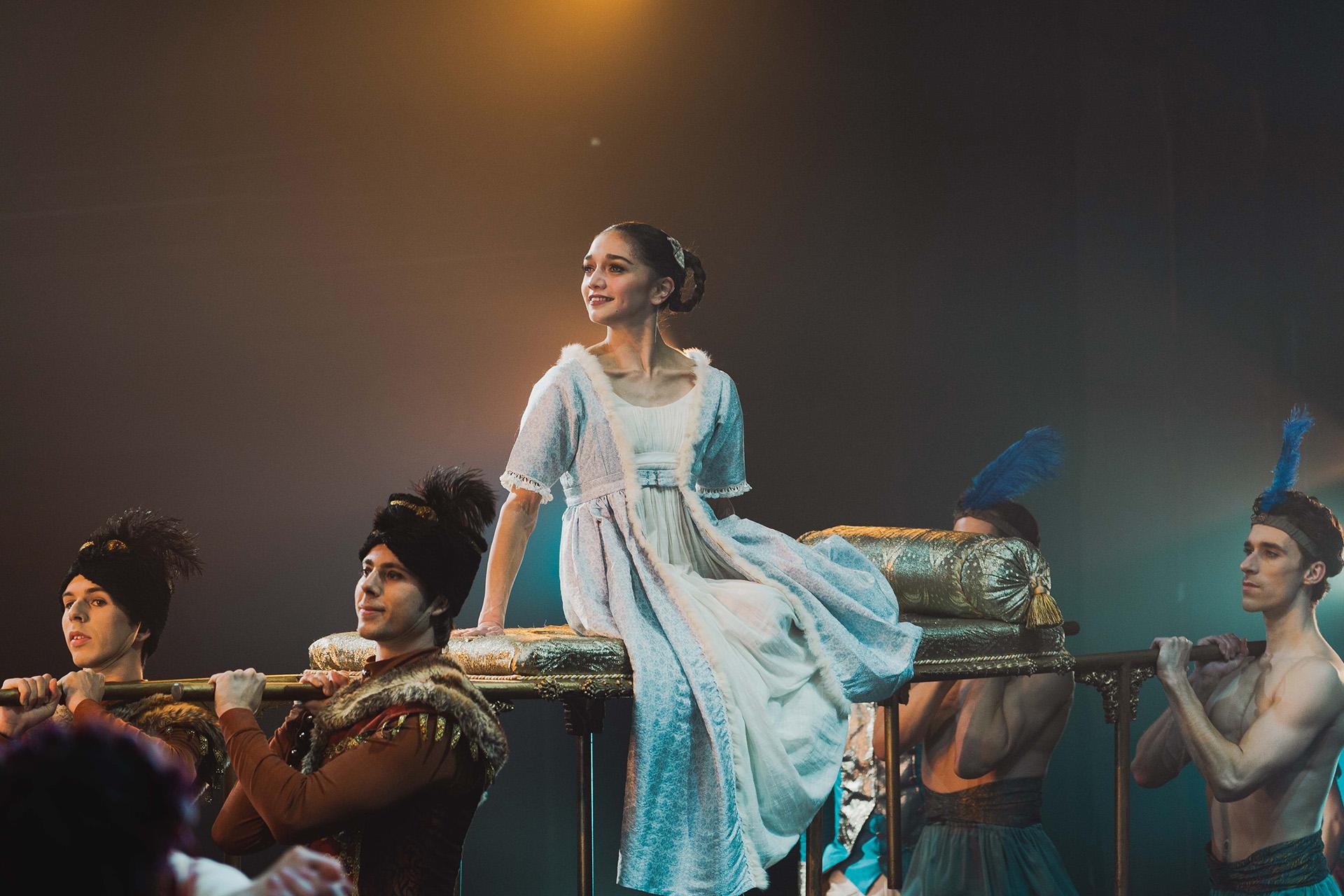 A young woman on a sedan chair held aloft on the shoulders of four dancers
