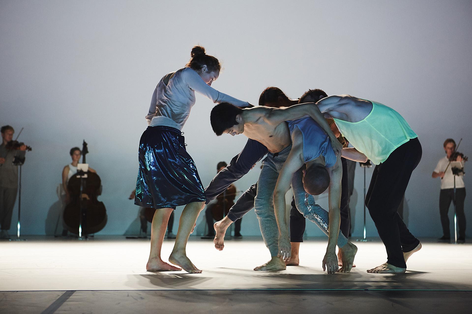 Five people pressed close to each other, one carries another on his back while the others support them