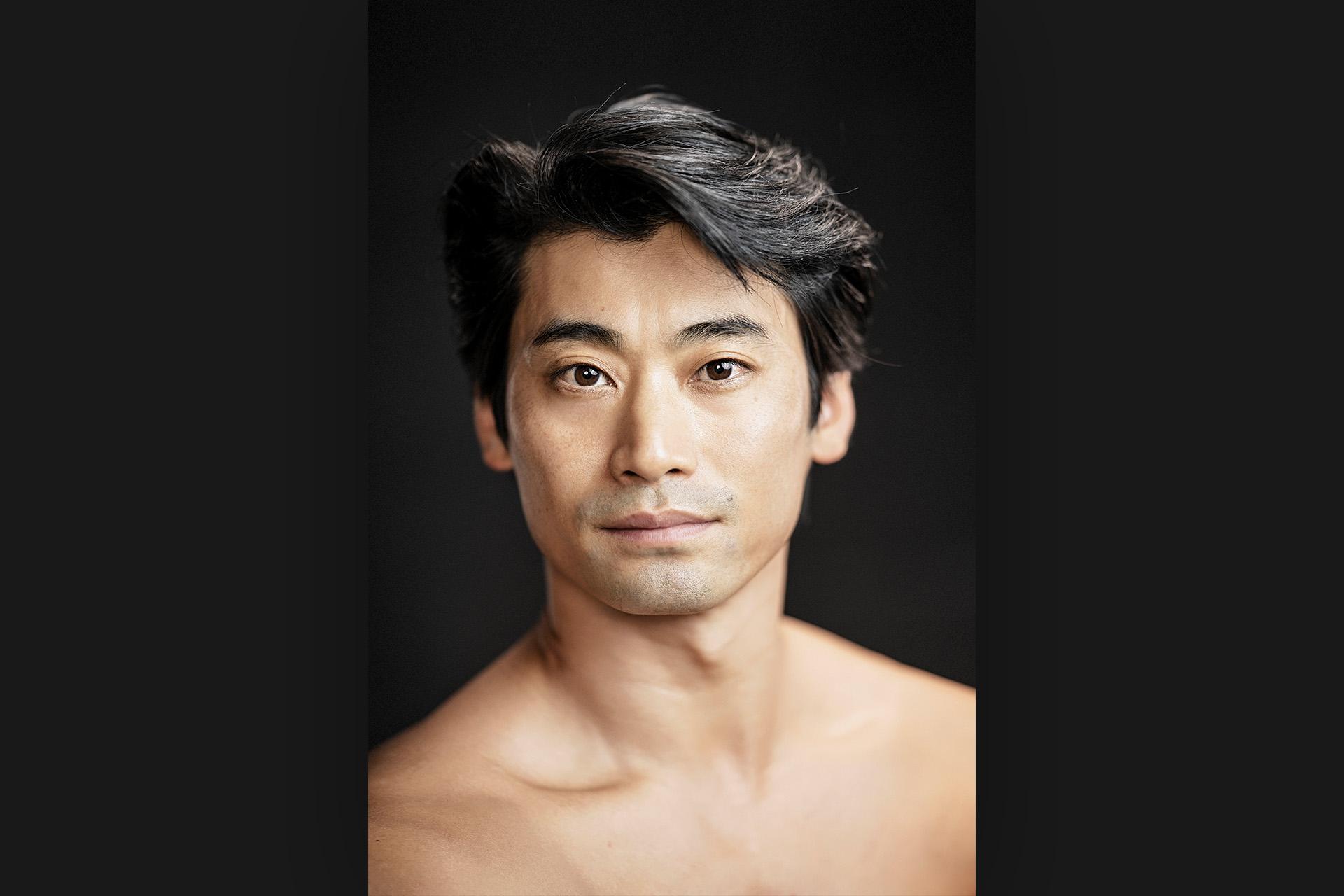 Photo of the head and shoulders of dancer Ryoichi Hirano against a very dark background