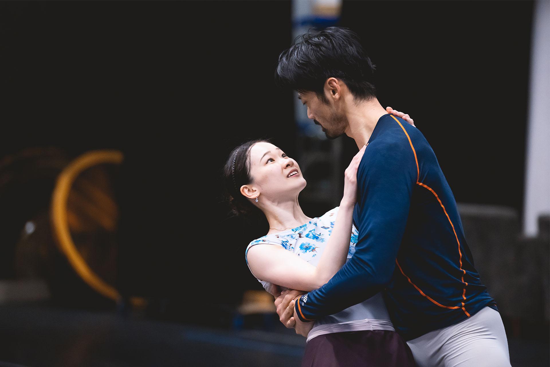 Dancers in rehearsal one dipping the other while holding her around her back and she has one hand over his right shoulder and the other hand placed on his chest