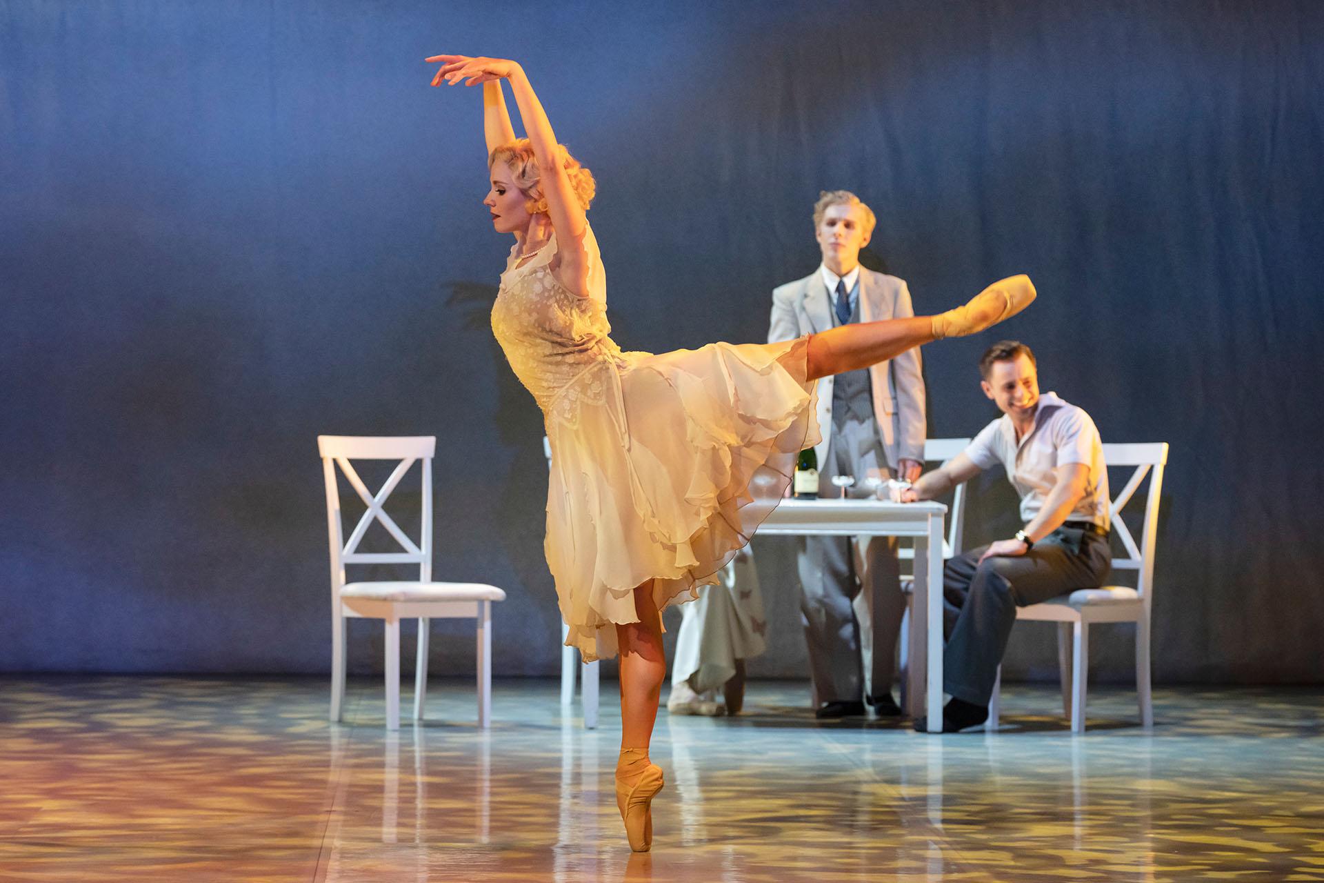 The Great Gatsby, production, 2023, dancer Dominique Larose. Photo Johan Persson Blonde female dancer in arabesque wearing a flowing white dress while a friend looks on