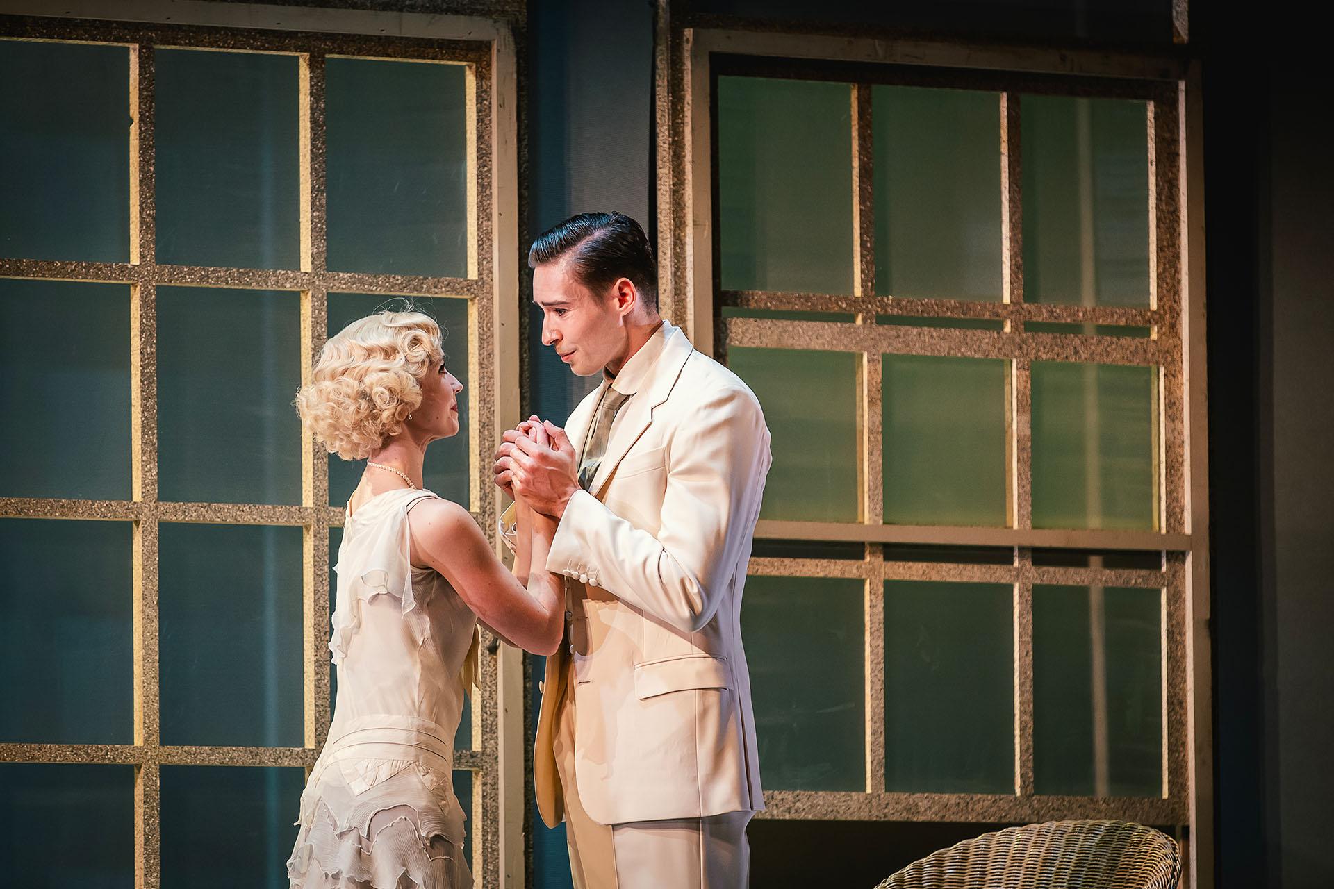 The Great Gatsby, production, 2023, dancers Dominique Larose and Joseph Taylor. Photo Emily Nuttall Two dancers dressed in smart white clothes gaze lovingly into one another's eyes whilst hold hands