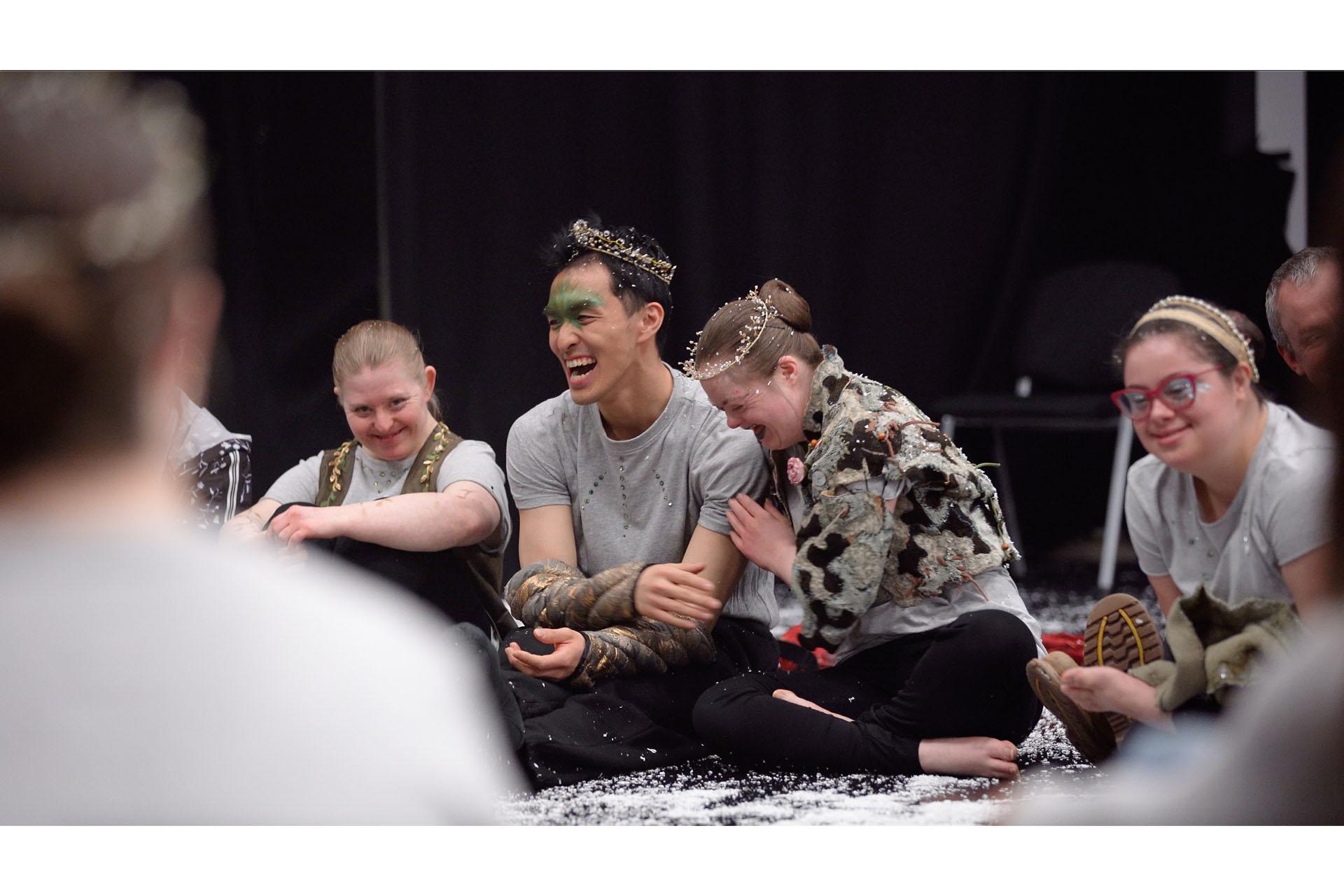Performers laughing and smiling together while sat in a circle on the stage