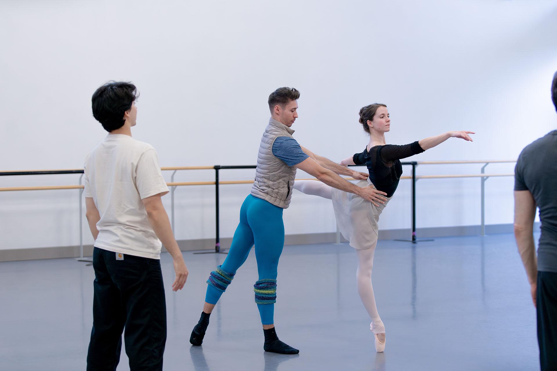 Dancers holding their pose while the choreographer looks on.
