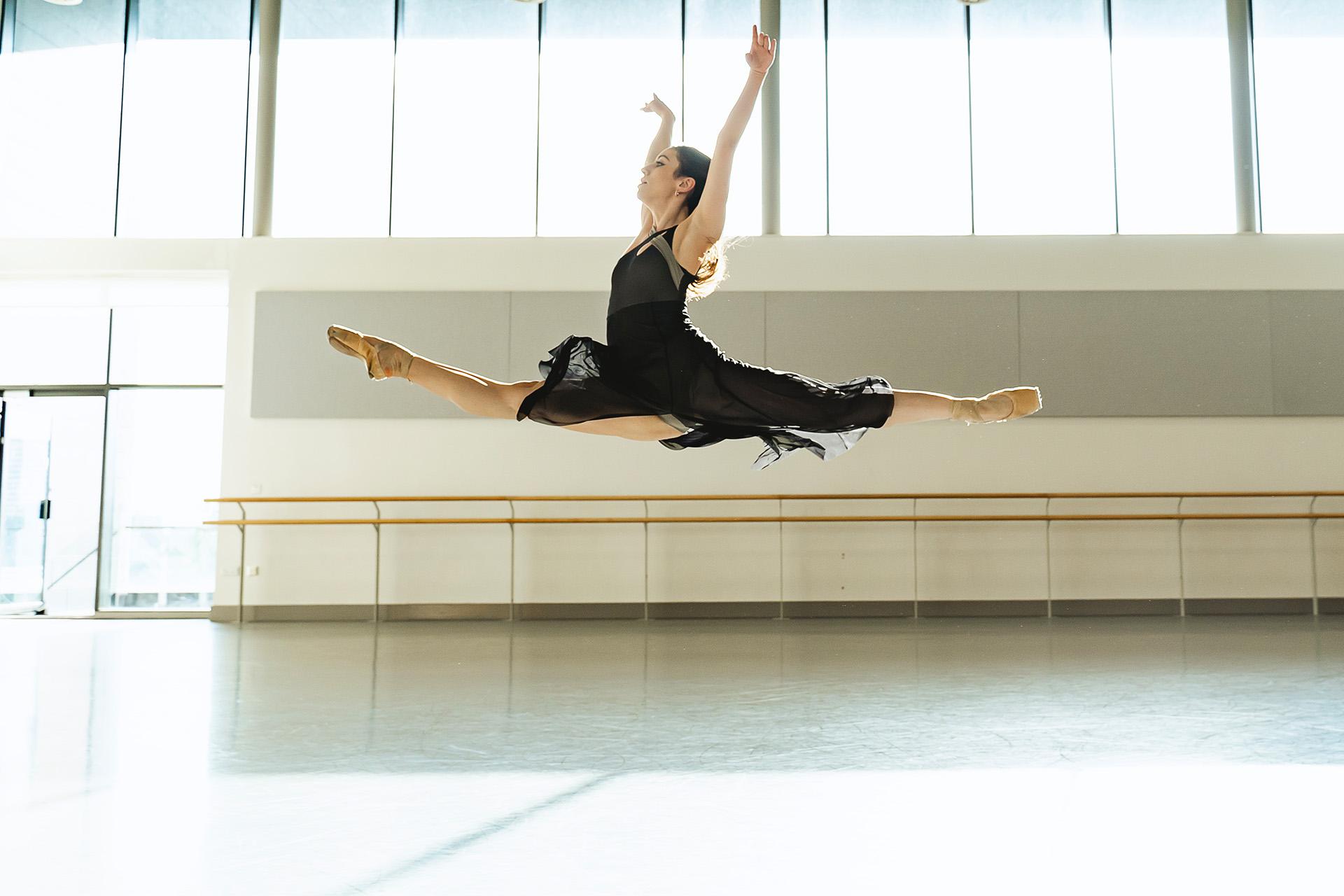 A dancer high in the air performing a grand jete with perfect grace.