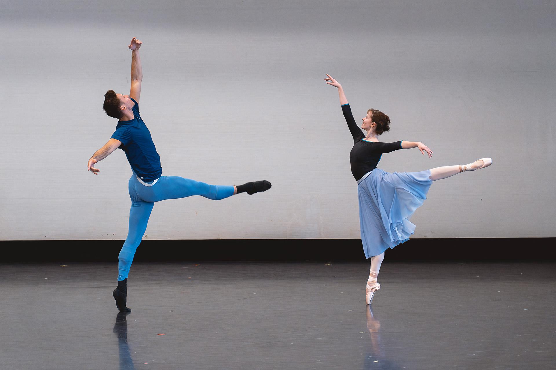 Two dancer striking similar poses, both on one leg, the male to the left has a leg perpendicular to his body in from of him, and the female to the right is perfectly arabesque