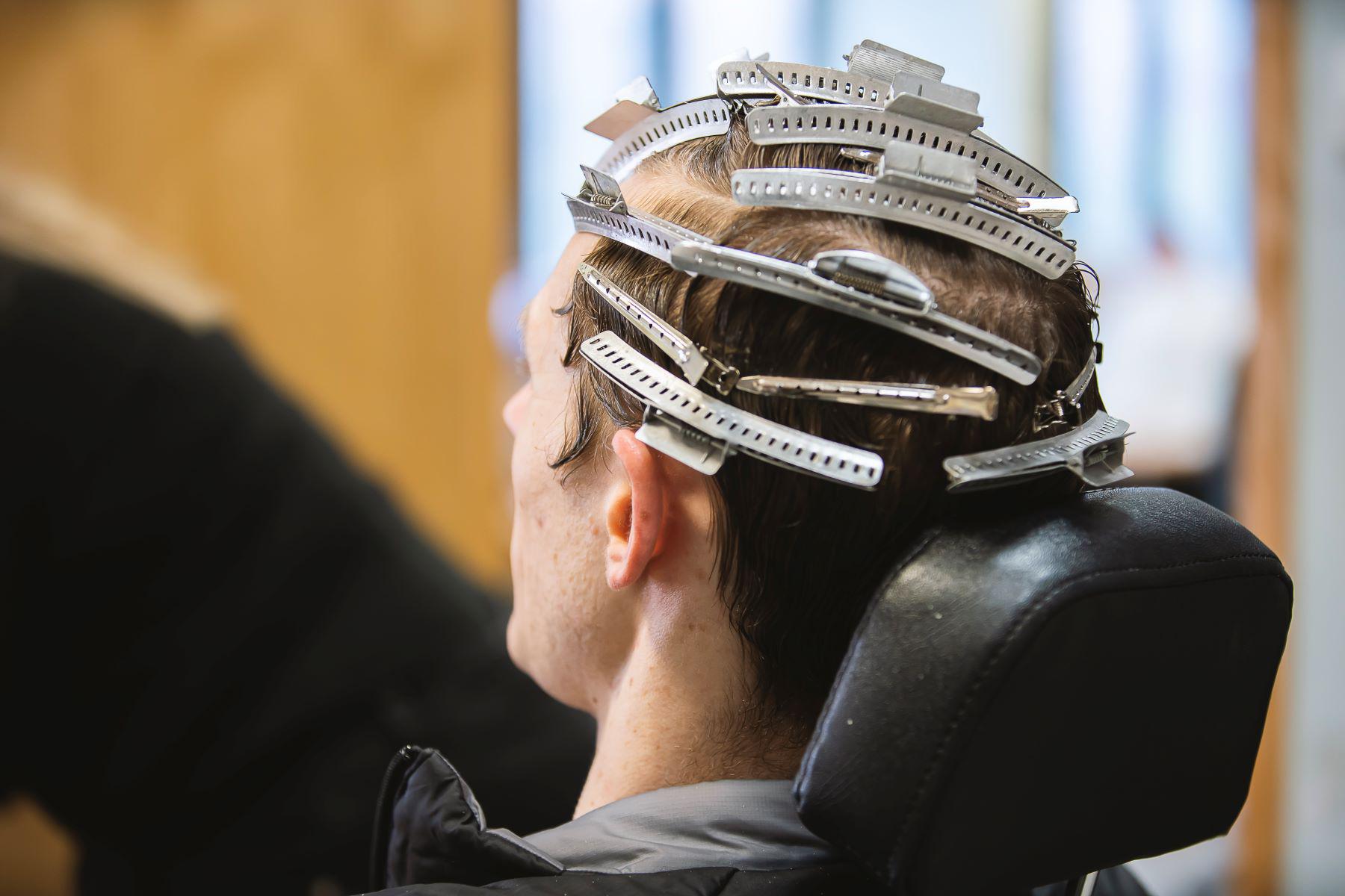 A male sits with hair curlers applied.