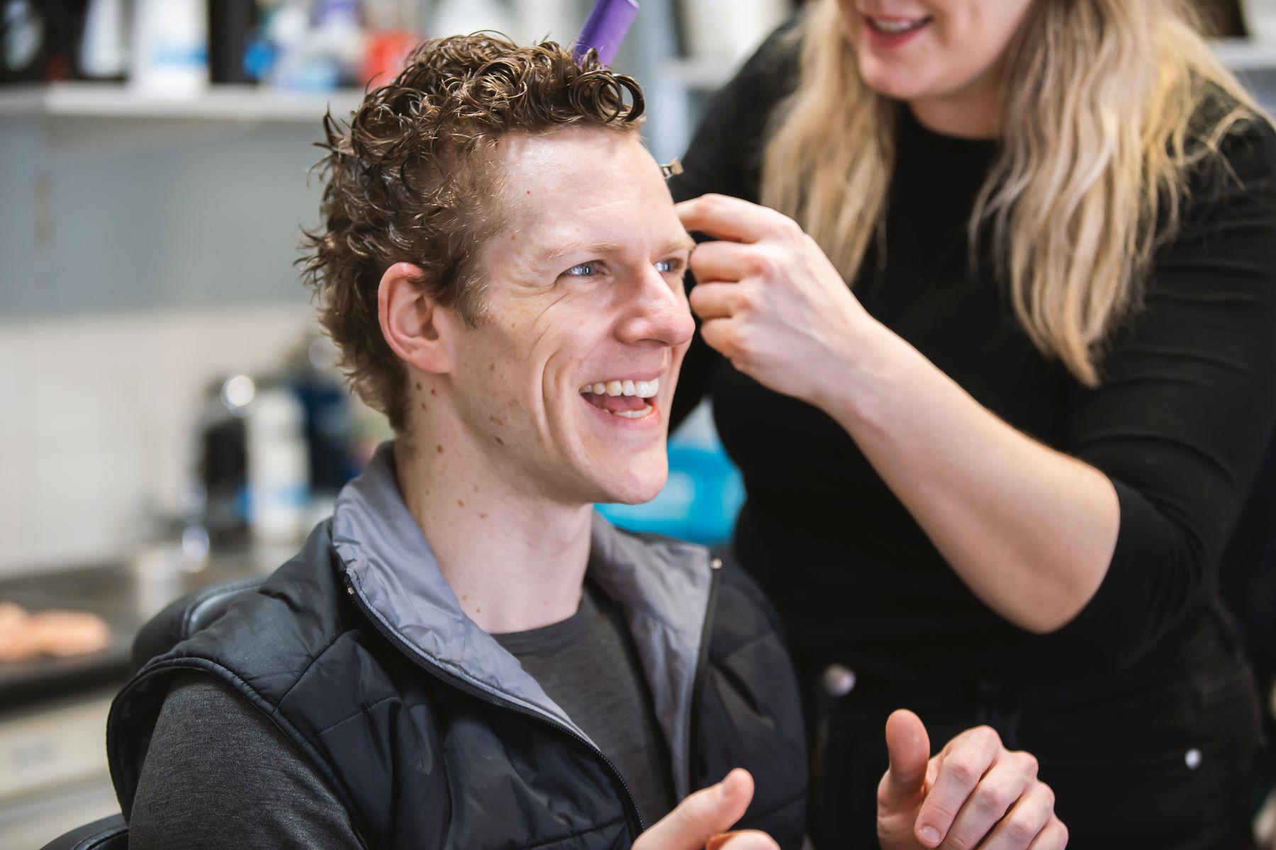 A female hair stylist works on a male dancer.