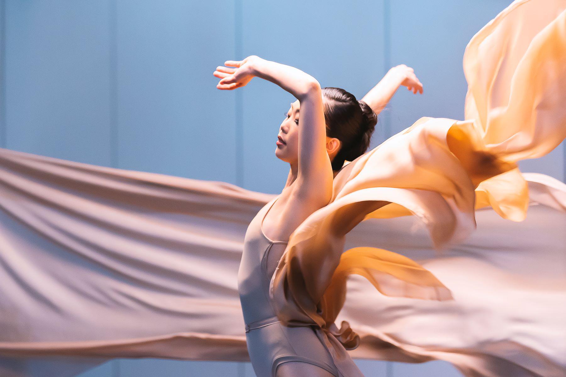 A female dancer waves her hands in the air as fabric blows around her