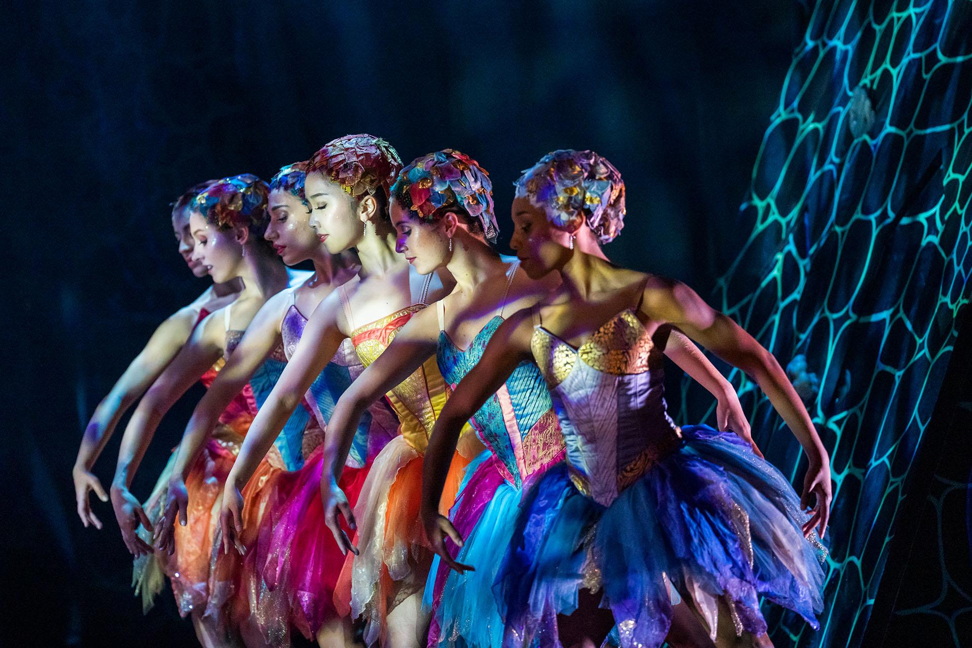 Beauty and the Beast, production, 2023, Northern Ballet dancers, photo Tristram Kenton Six female dancers, each wearing brightly colourful dresses and hats stand in a row looking down