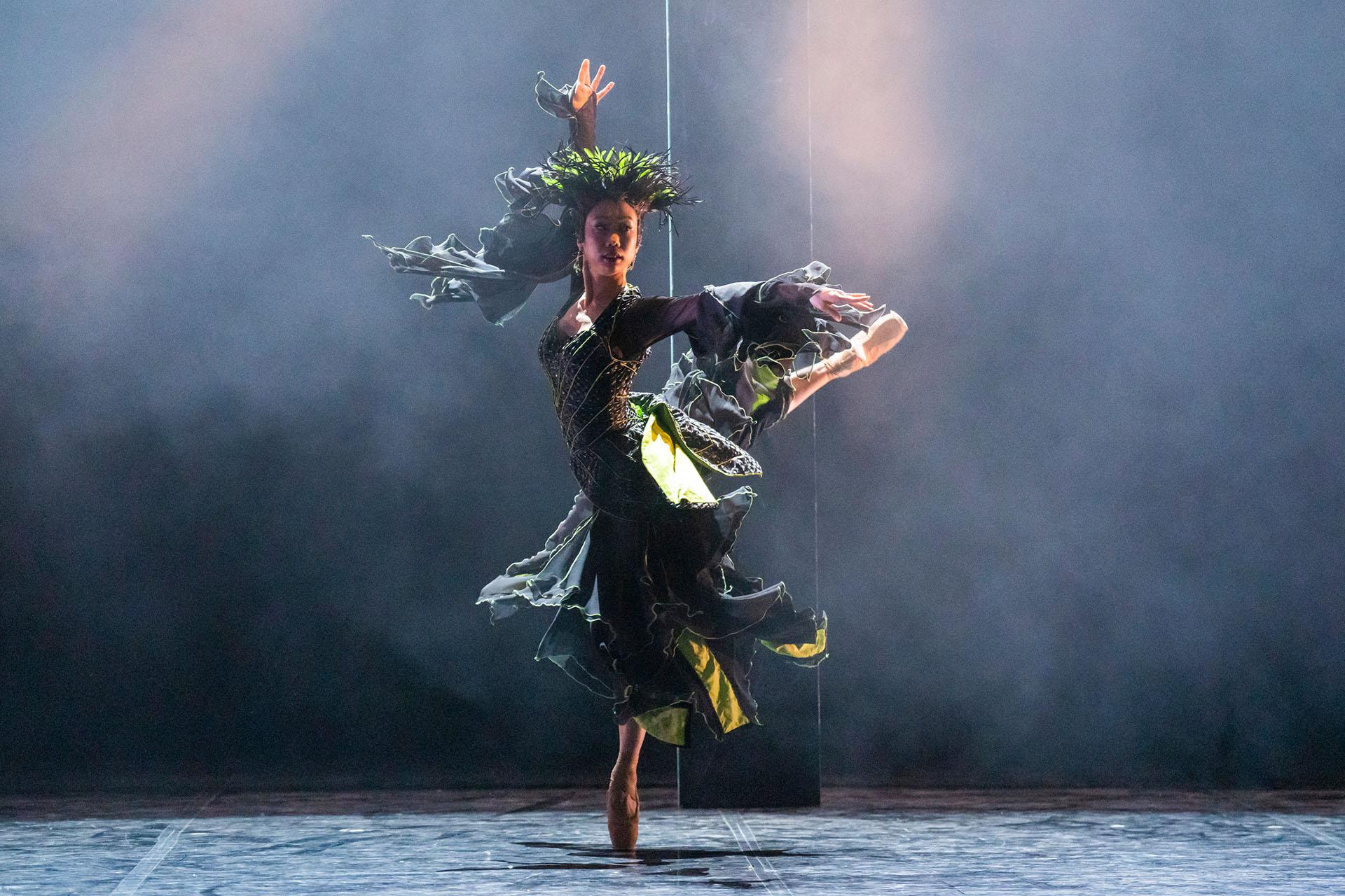 Beauty and the Beast, production, 2023, dancer Sara Chun, photo Tristram Kenton La Fée Magnifique standing on one foot en pointe, a leg raised behind her, one arm above her, her black and green dress spread out by the force of her spin.