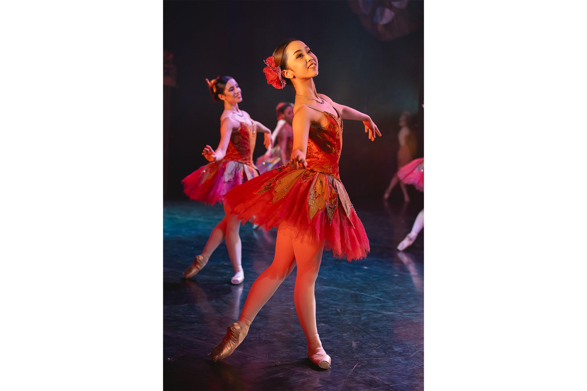 Woman in red/pink ballet outfit stands posing elegantly, smiling wanly