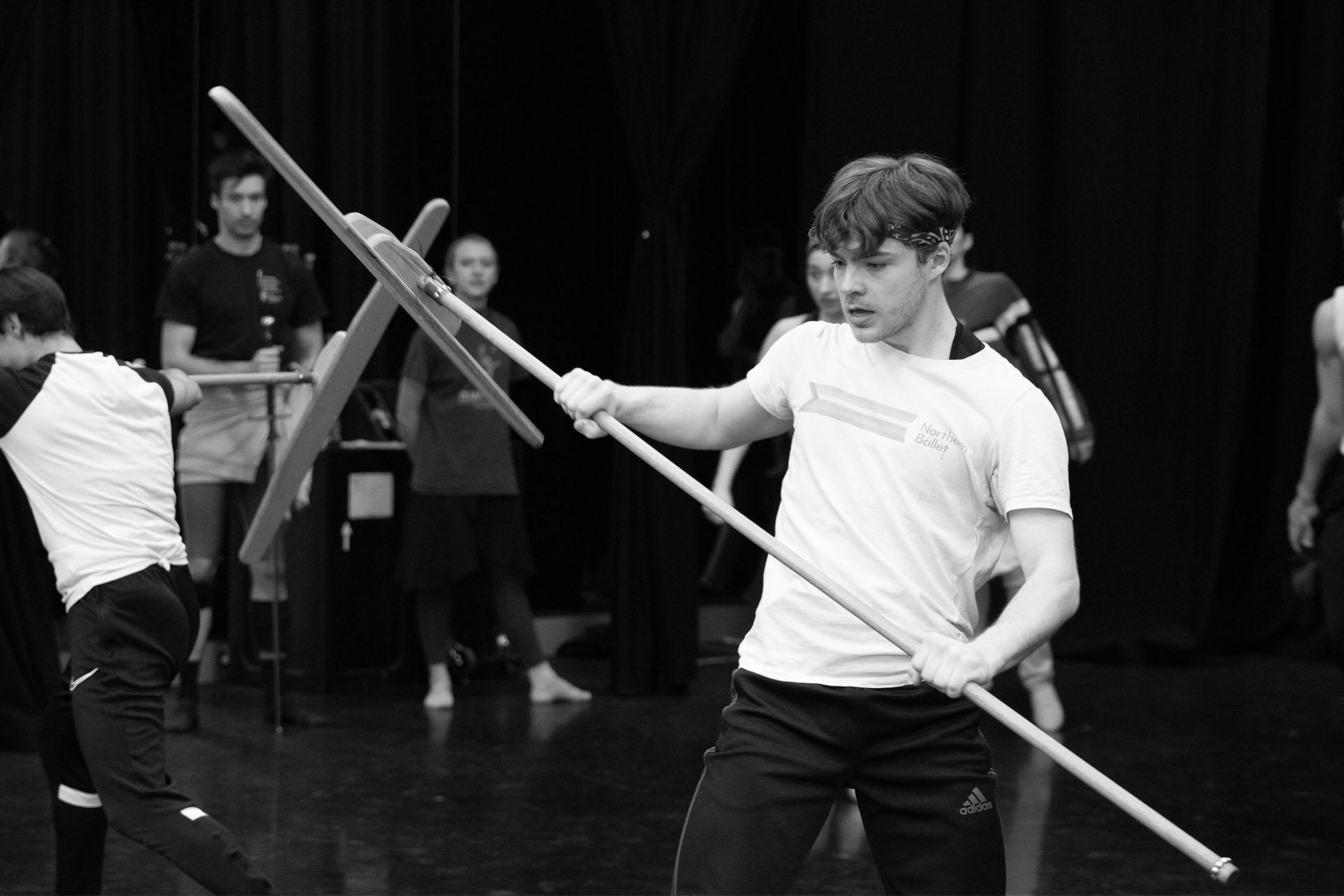 Black and white photo of a dancer holding a staff in rehearsals