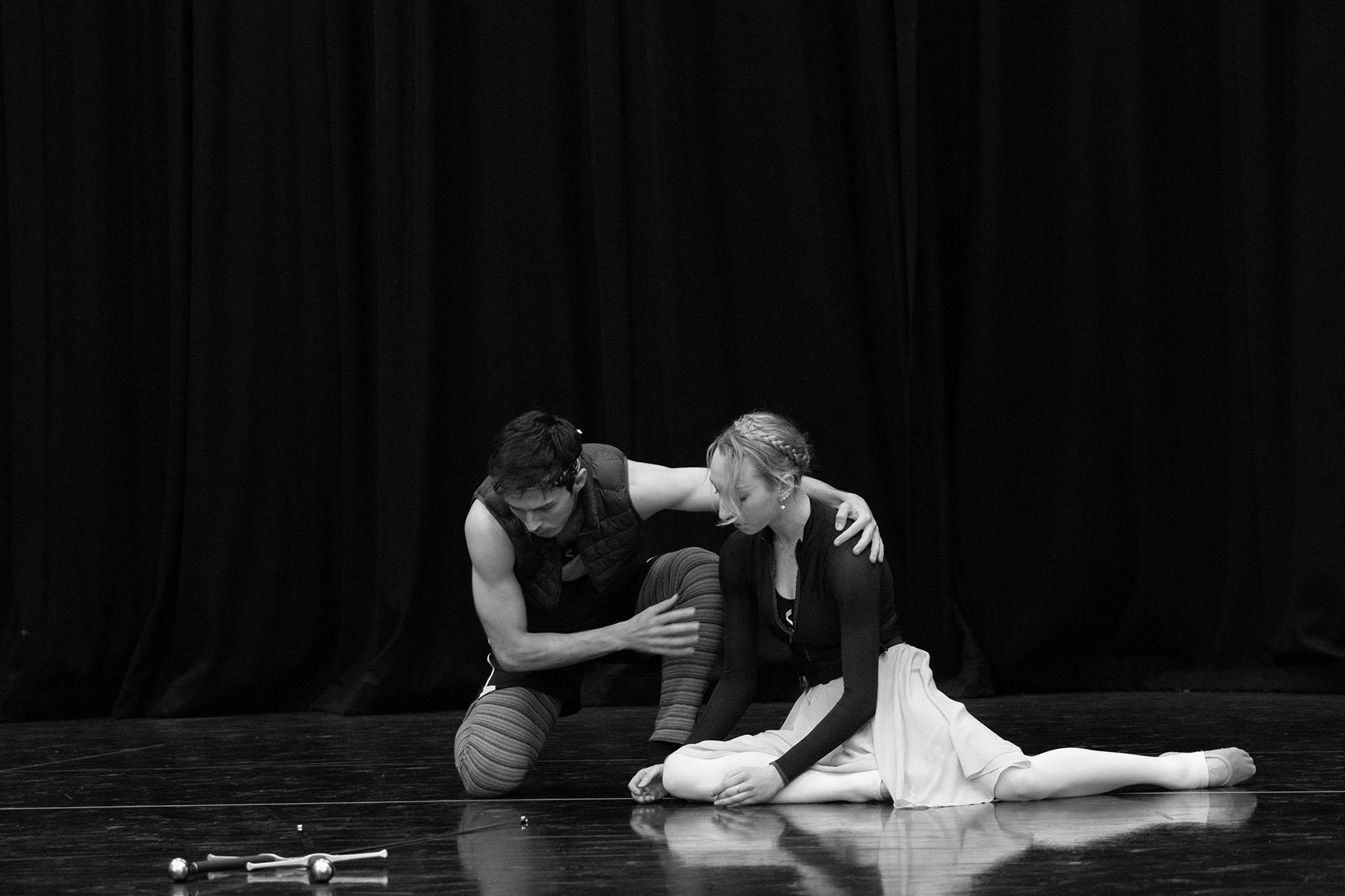 Black and white photo with a woman sat on her knees looking dejected and a man with an arm over her shoulders