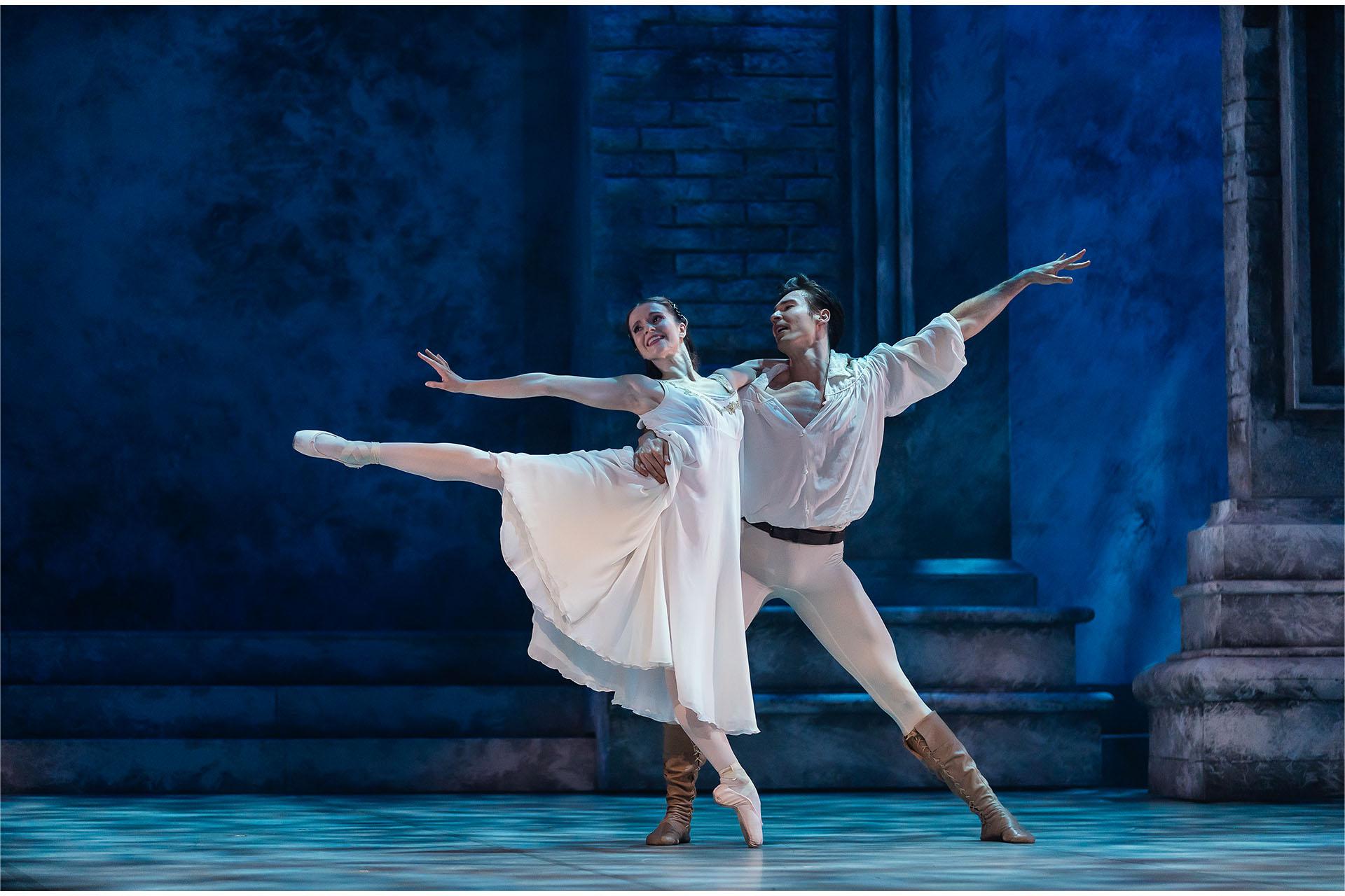 Romeo and Juliet stand facing out from the stage each with an arm holding the other