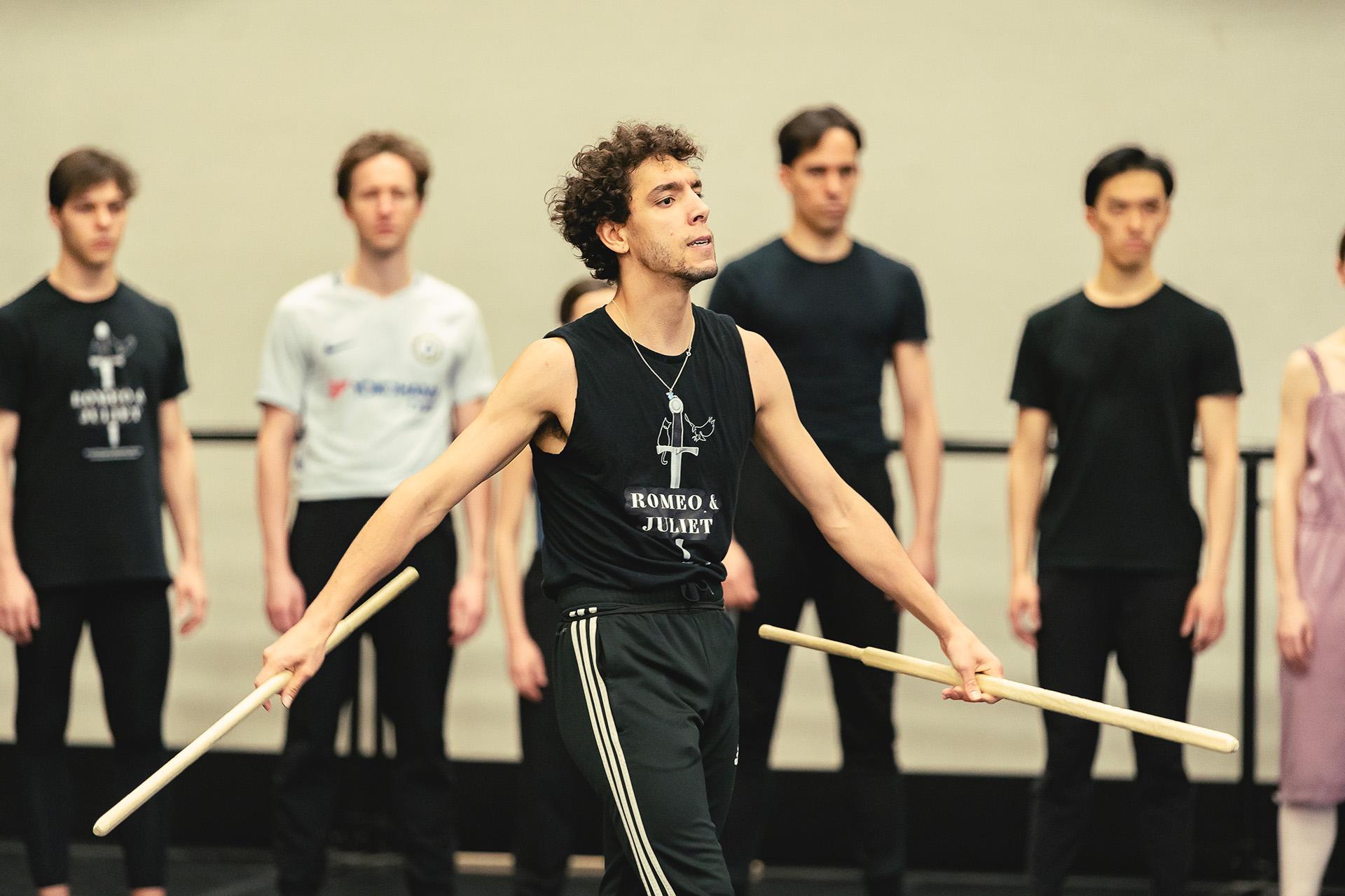 Dancer strides confidently across the stage with a weapon in each hand, is arms slightly spread threateningly