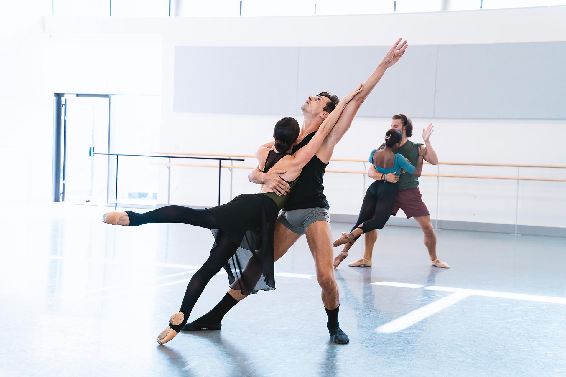 Two dancers in rehearsal, one surdy on his feet and the other leaning body against him whilst en pointe
