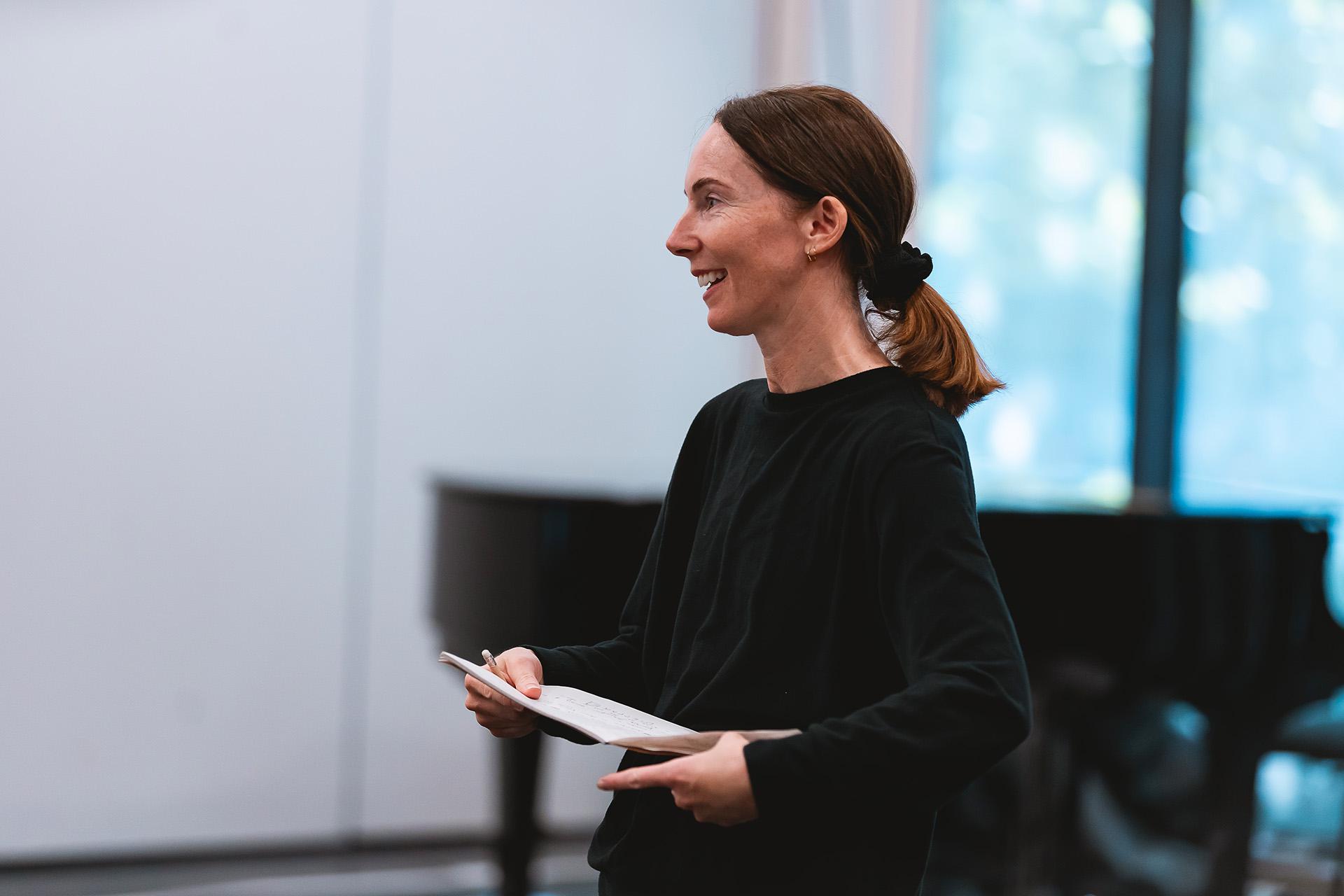 Smiling choreographer with medium-length hair holding a card.