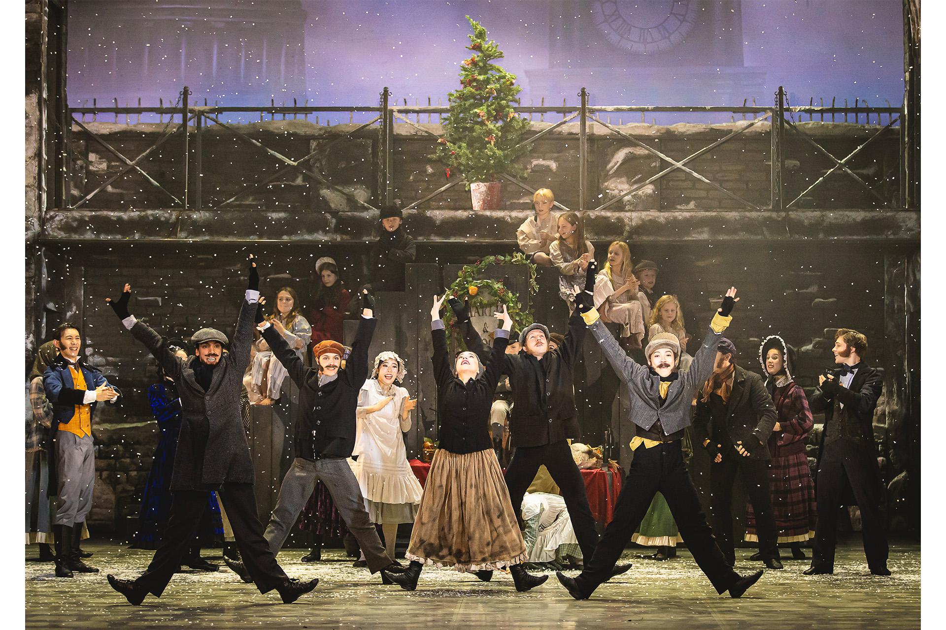A Christmas Carol, 2024, production, Northern Ballet dancers, photo Emily Nuttall Townspeople dance with their arms in the air and legs spread apart as snow falls.
