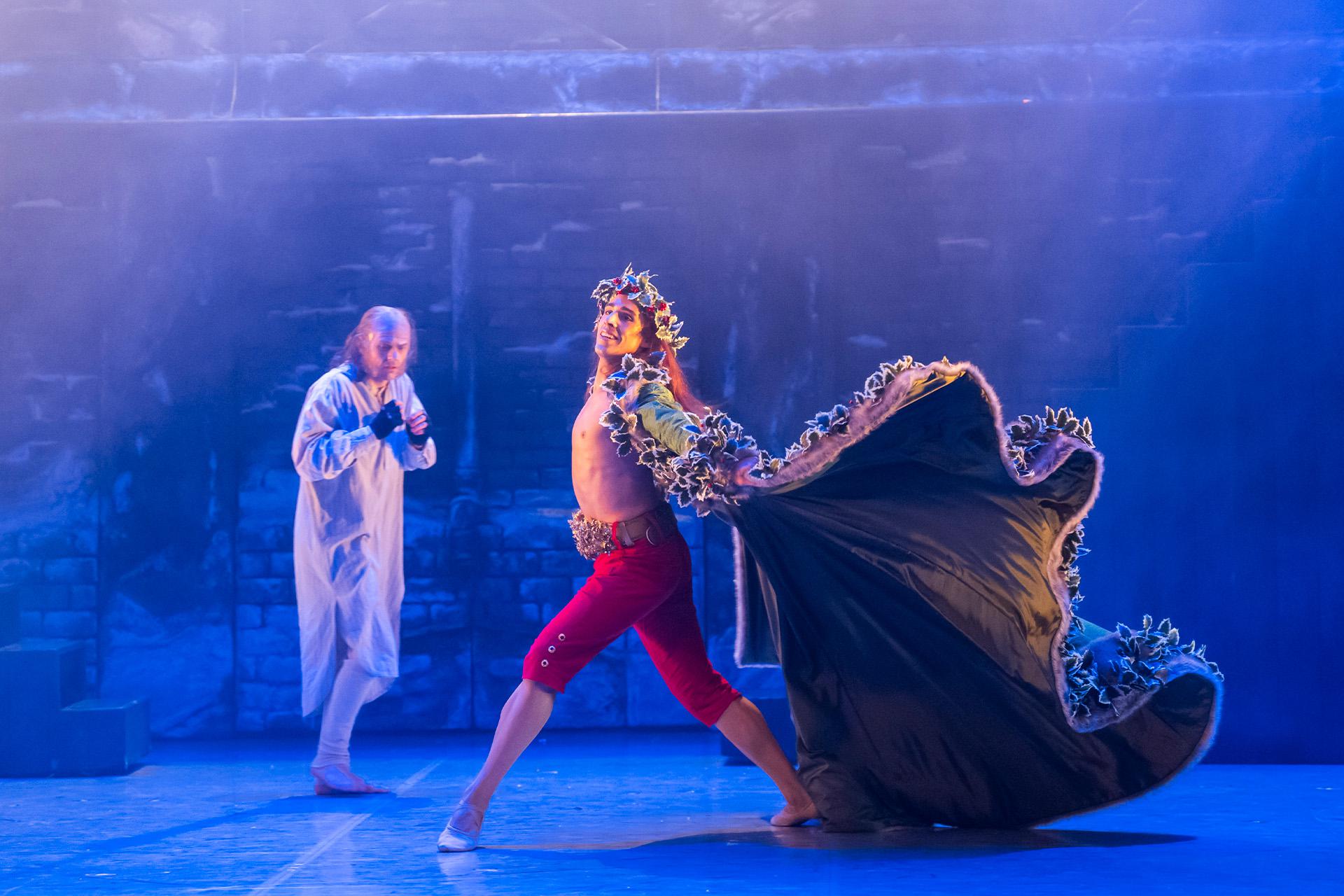A Christmas Carol, 2024, production, dancer Harry Skoupas and Jonathan Hanks, Photo Tristram Kenton The Ghost of Christmas Present strides past Scrooge, his cape billowing.