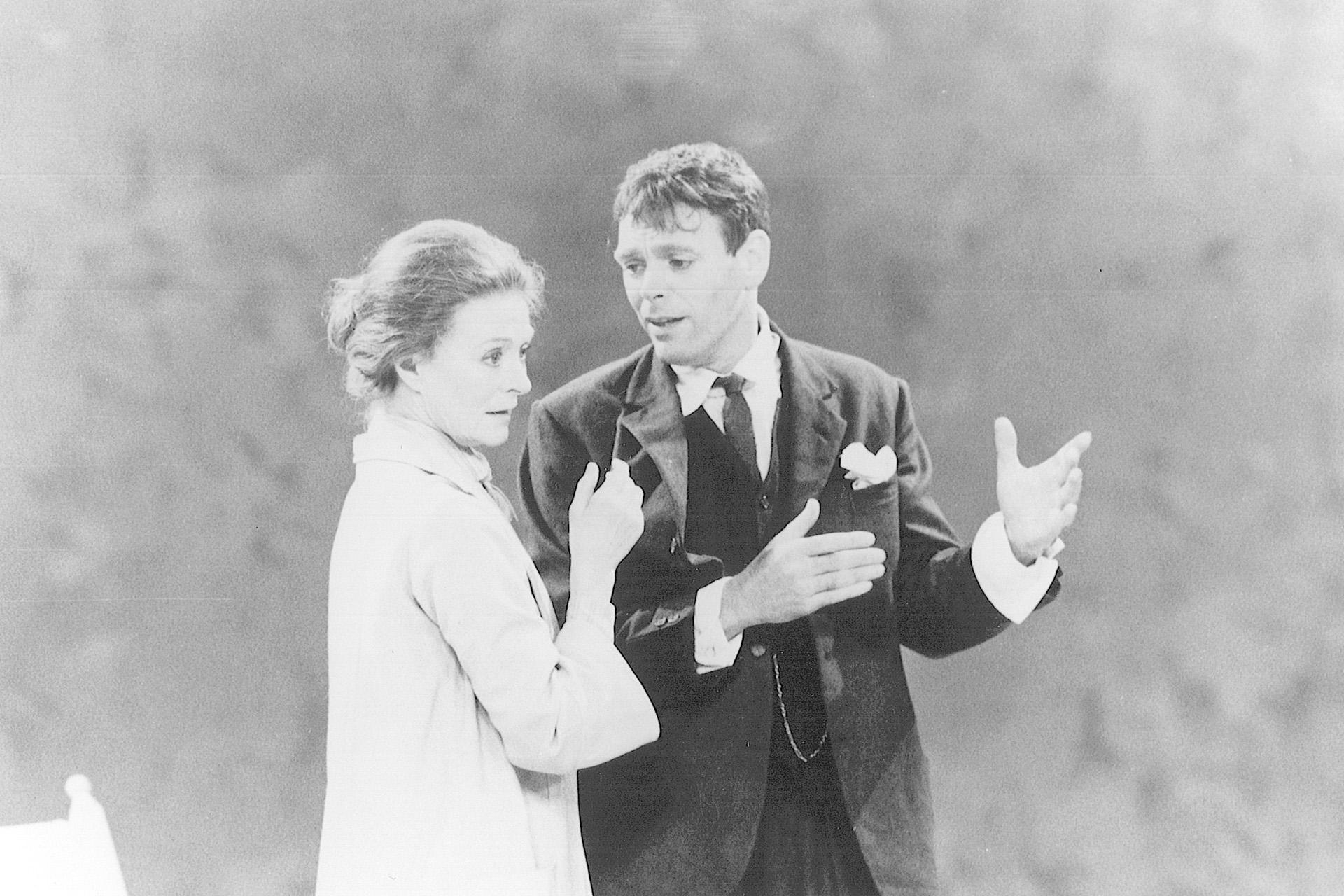 A black and white photo of two people from the waist up. One is in a light coloured jacket and the other a dark suit