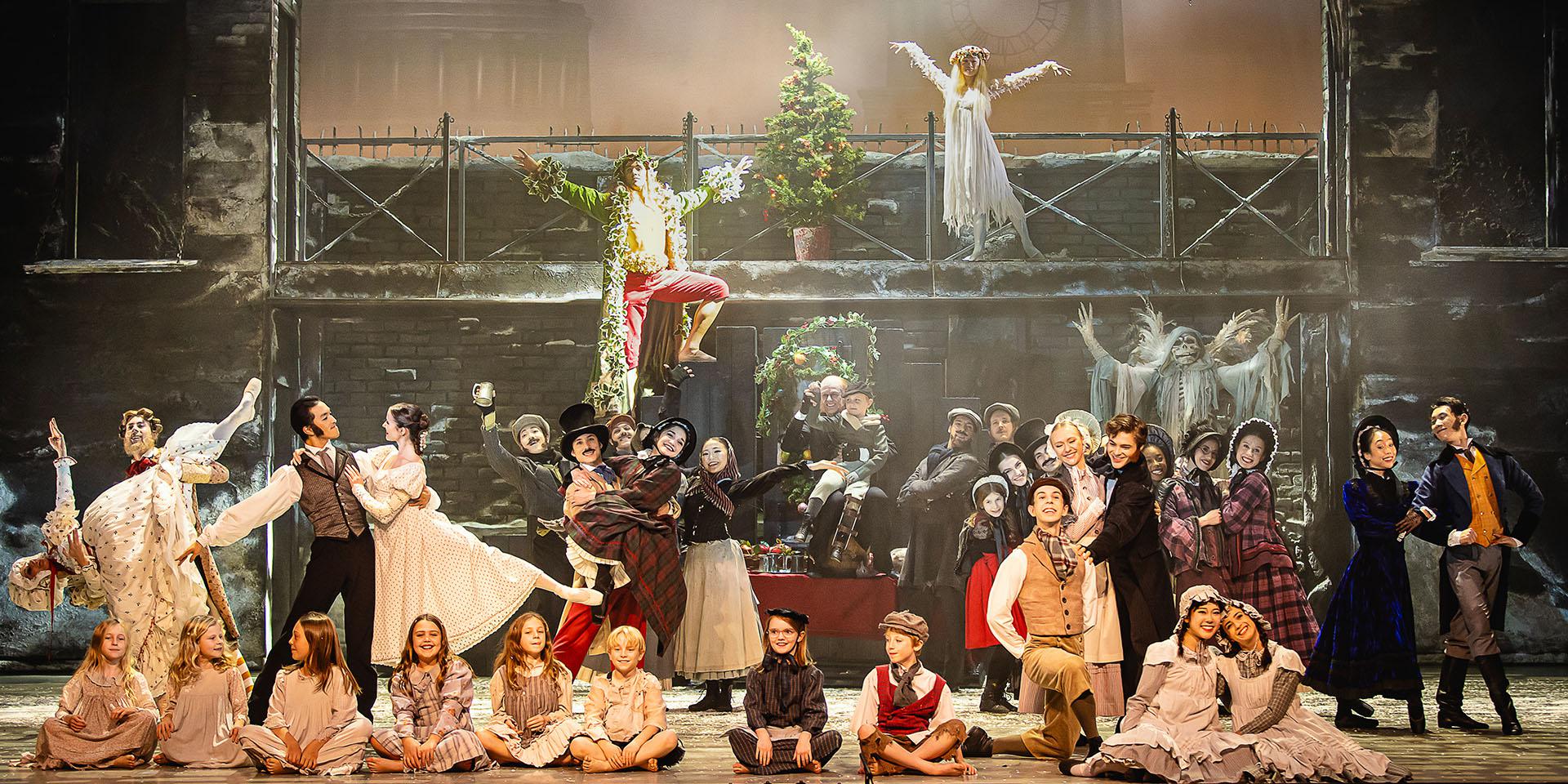 A group shot of dancers on stage smiling warmly in Victorian era clothing