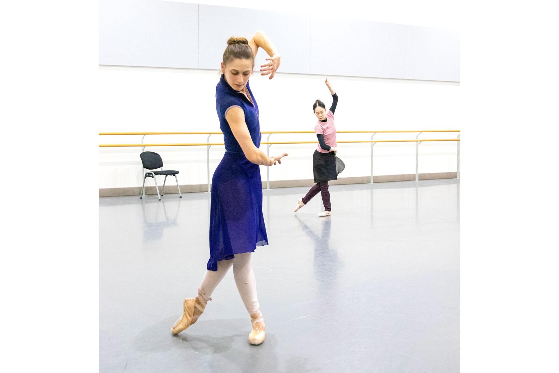 Dancer in a blue skirt and top, in pointe shoes, arms held in front of her making a square shape