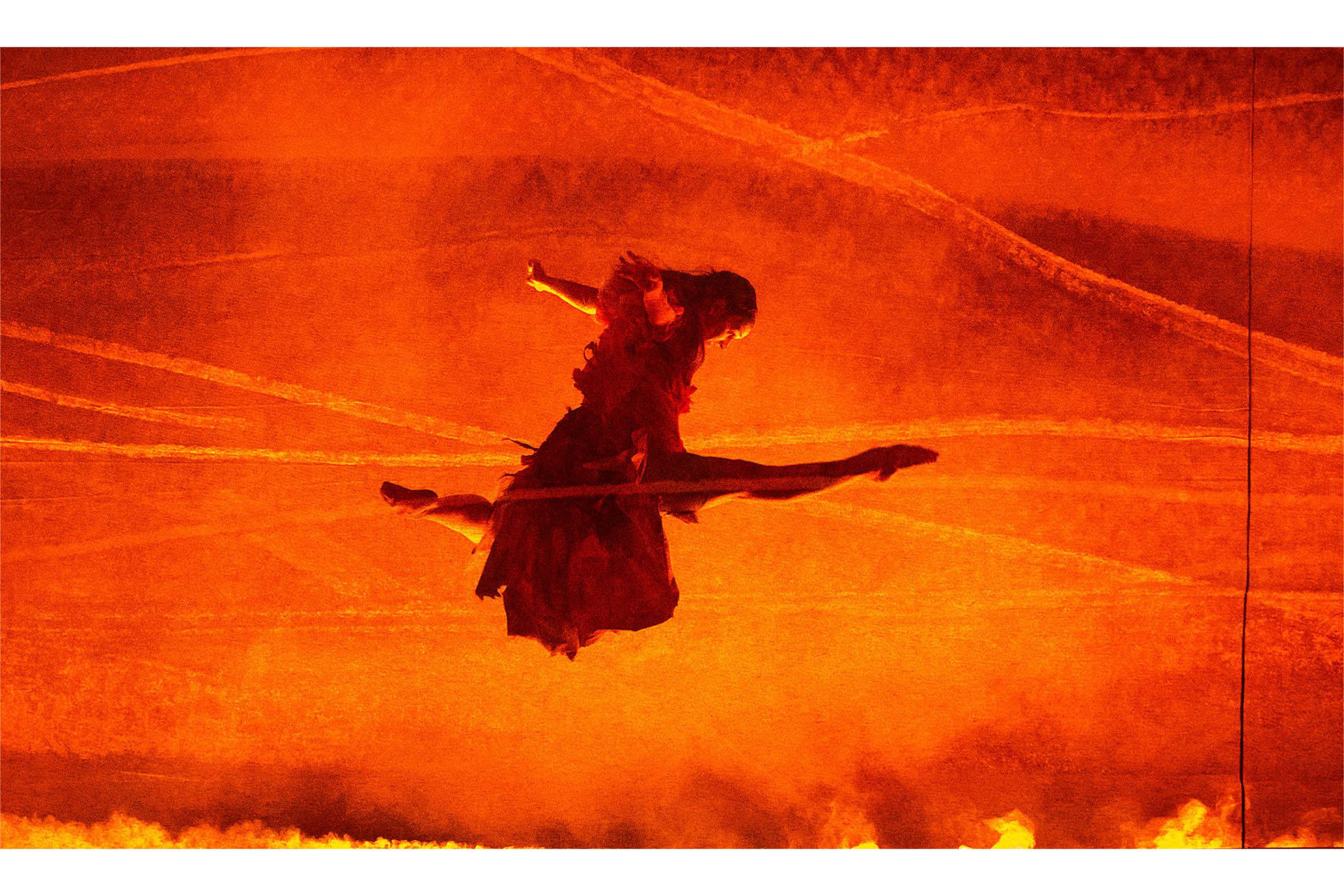 Jane Eyre, production, 2025, dancer Amber Lewis. Photo Emily Nuttall Lit by the orange hue of flames, a dancer performs a great leap
