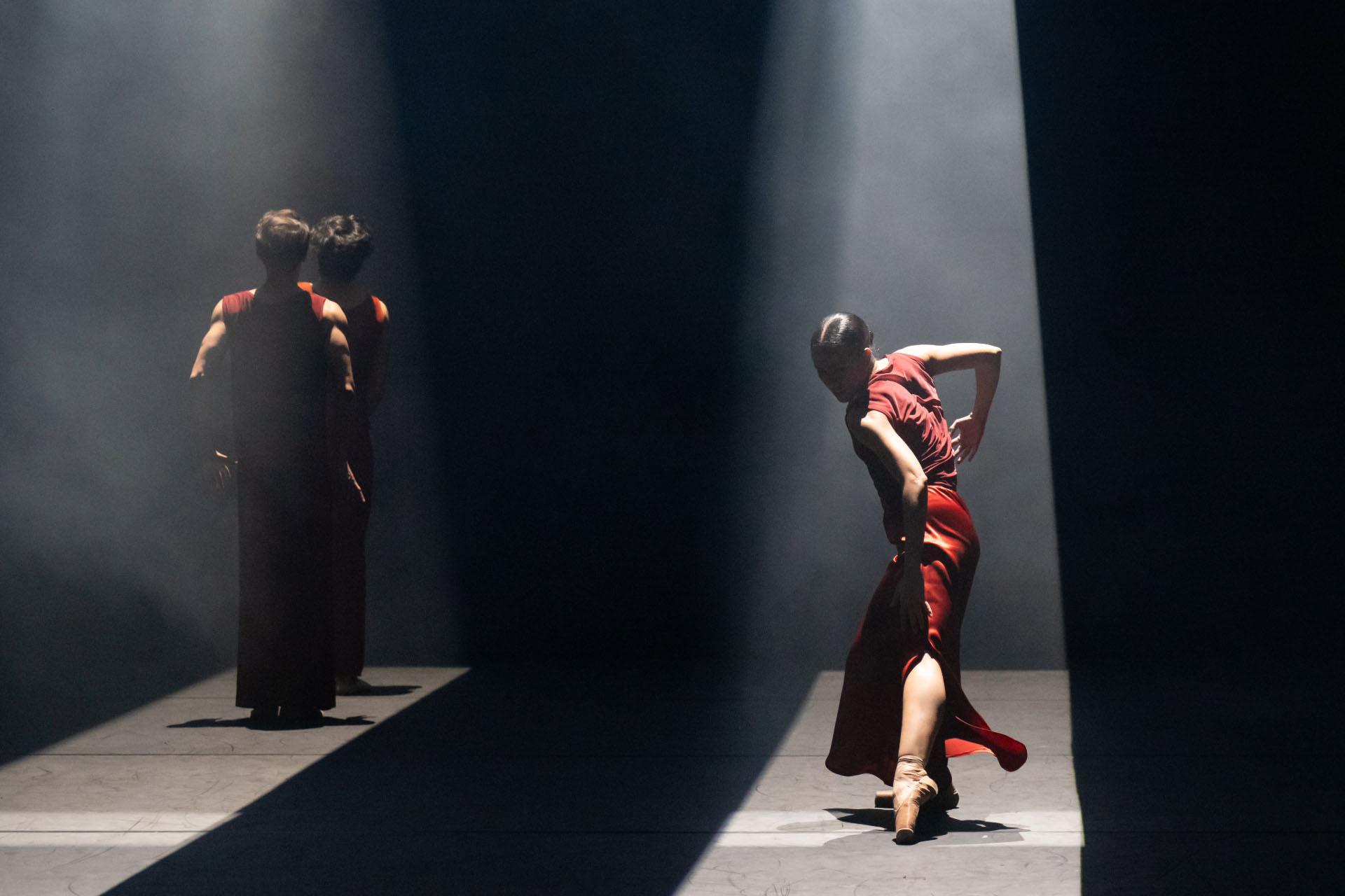 Bath in a shaft of light from above, a woman in a red dress pointes a foot forward provocatively