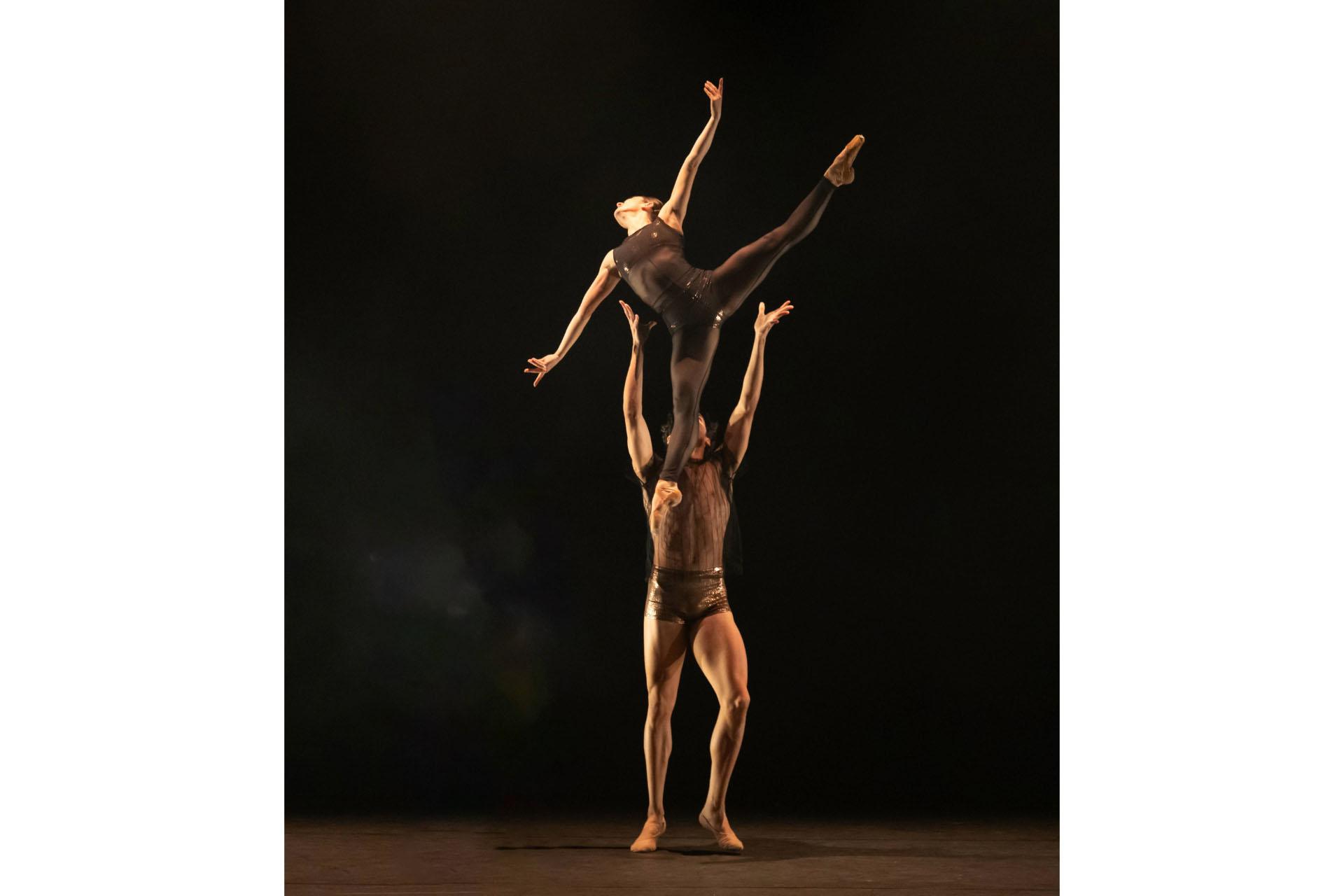 Two dancers, one lifting the other over his head, the lifted dancer holding the legs and arms apart.